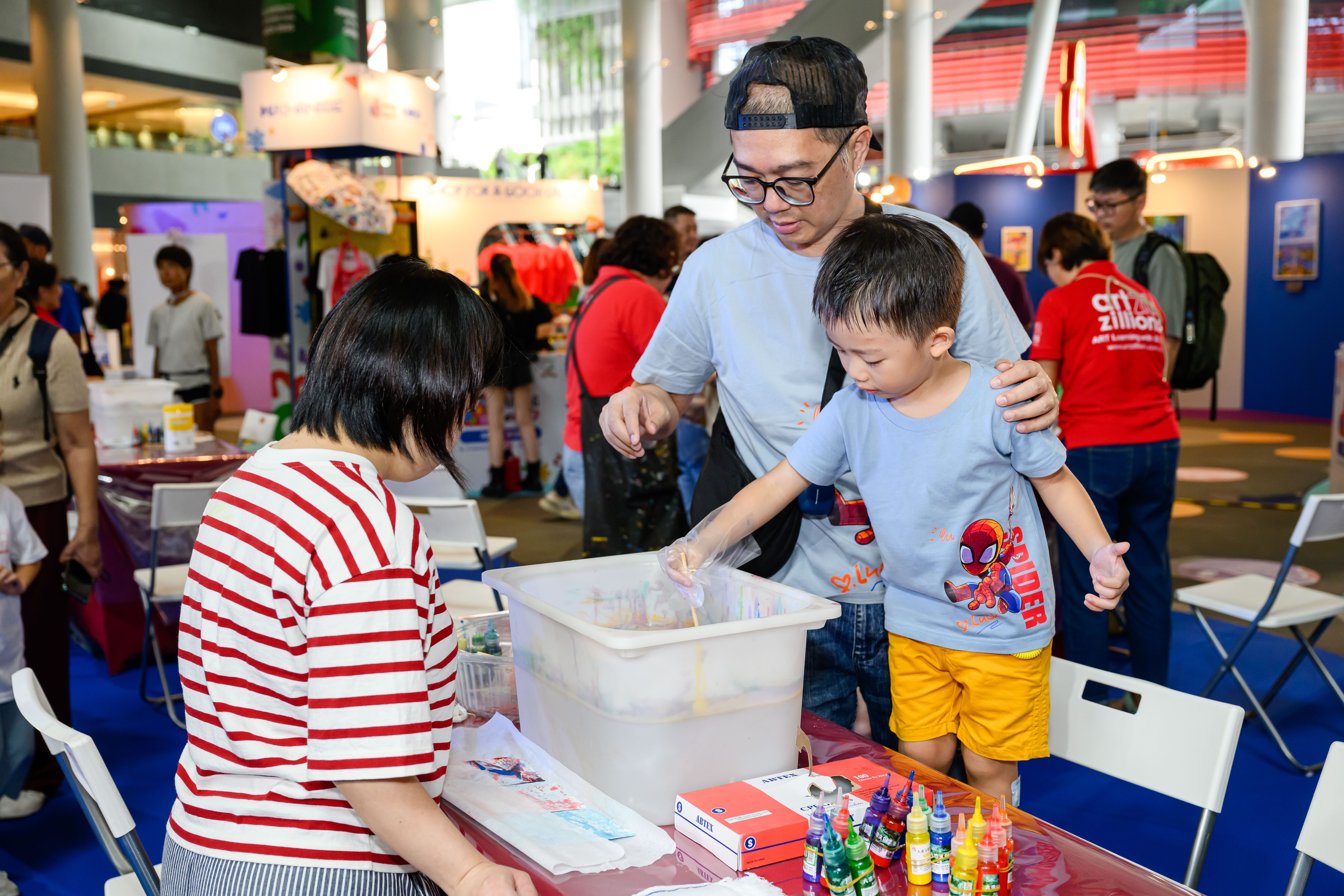 Father and son adding coloured dyes into a container of water while a guide observes them.