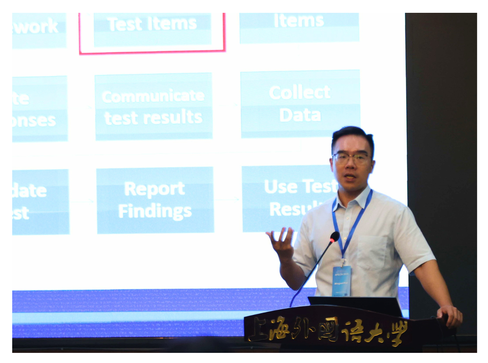 A person stands at a podium presenting in front of a screen with various project management steps.