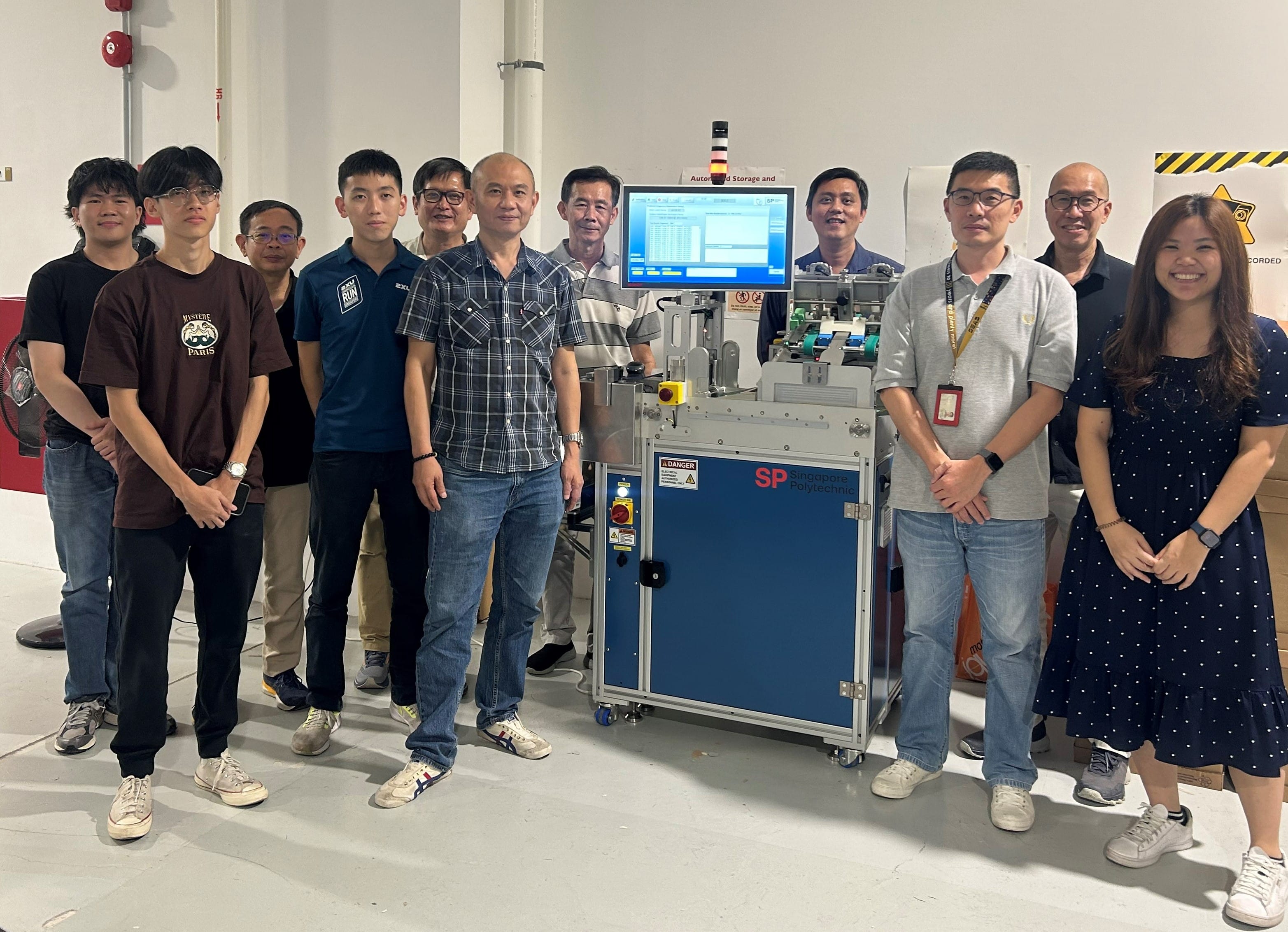 A group of people stands in front of a machine with a blue panel and a screen displaying data.