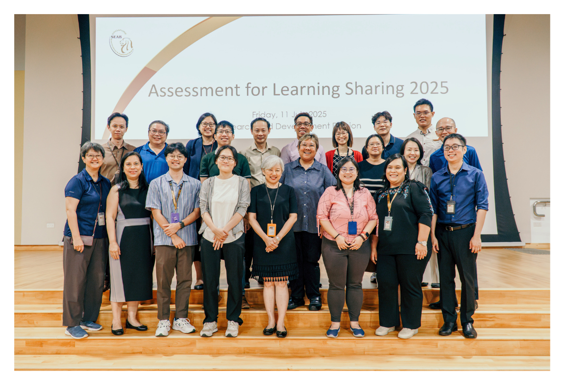 A group of people stand on steps in front of a large "Assessment for Learning Sharing 2025" sign.