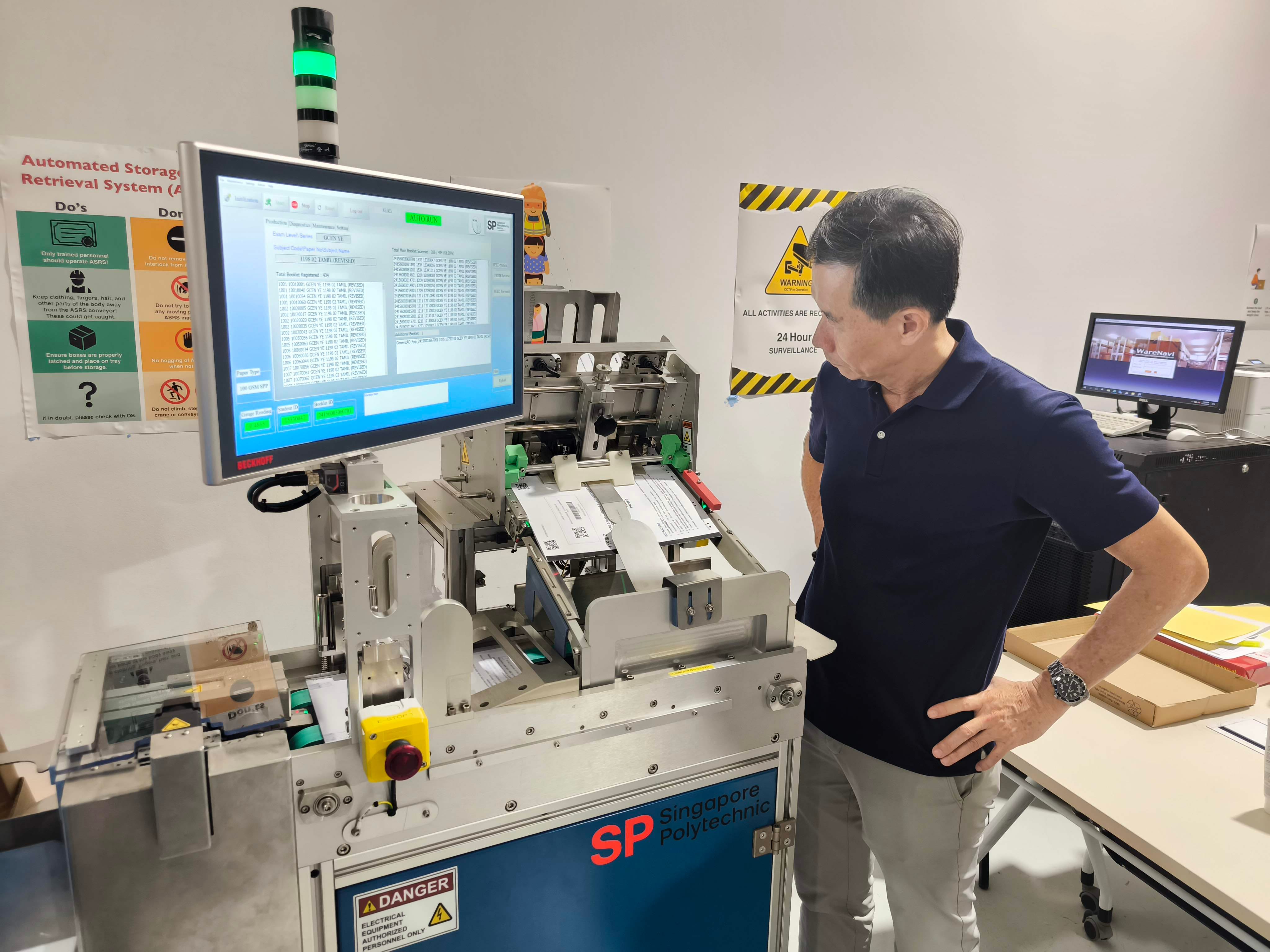 An individual wearing a navy shirt observes a machine labeled "Singapore Polytechnic" with a screen displaying data and controls.