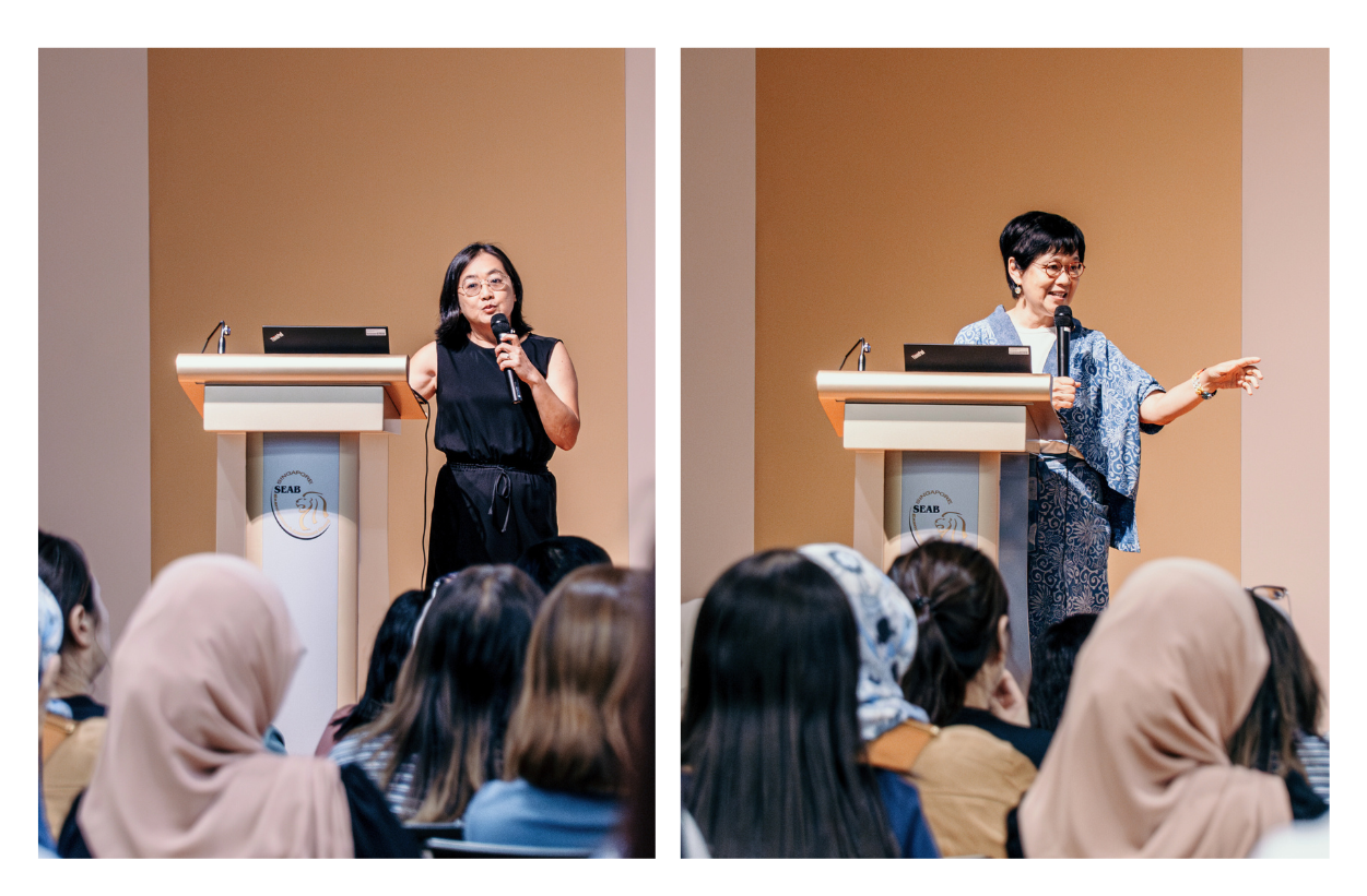 Two presenters stand at podiums speaking to an audience in a conference room.