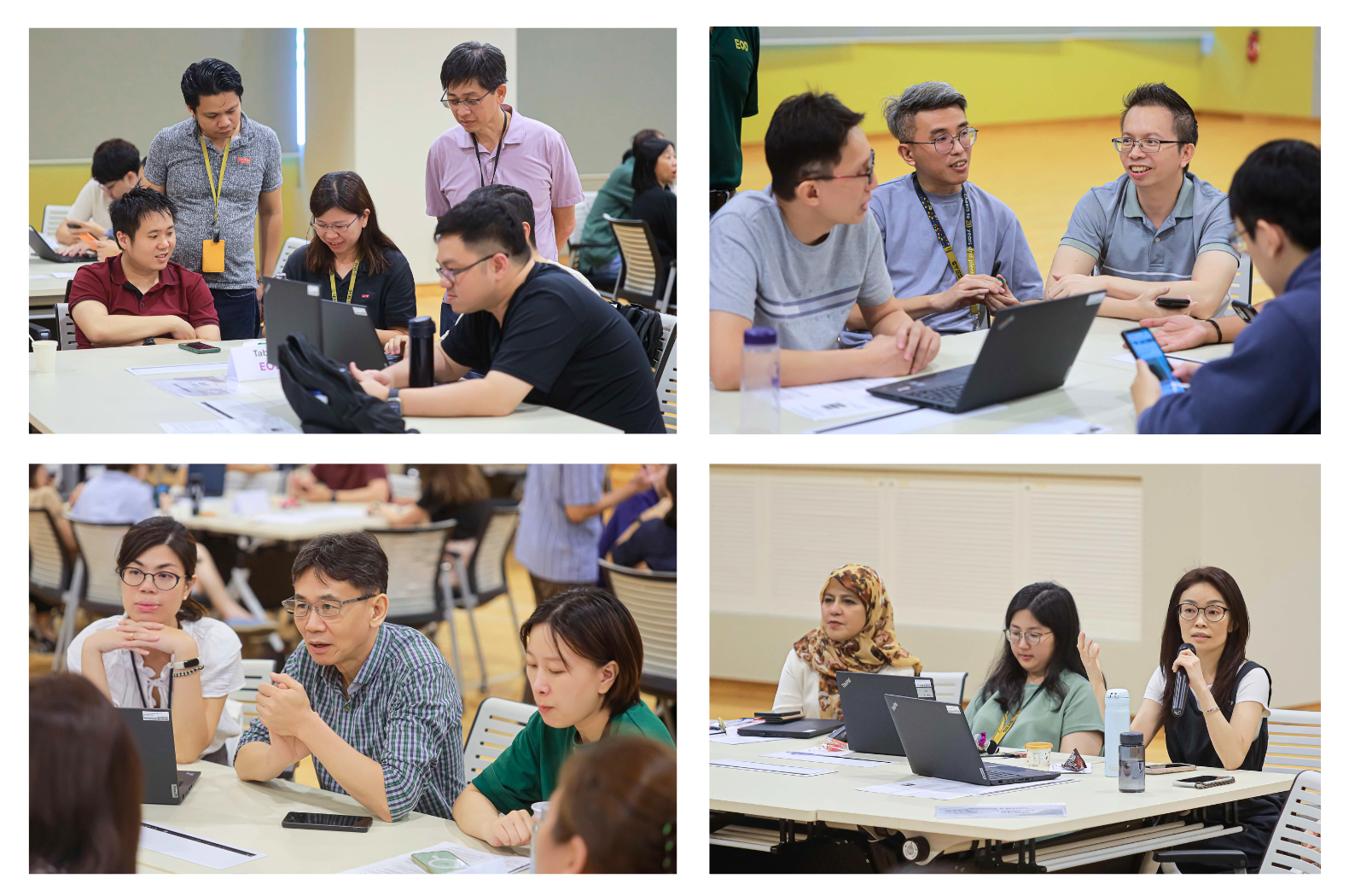Groups of people are working and discussing around tables with laptops and documents in a classroom or meeting room.