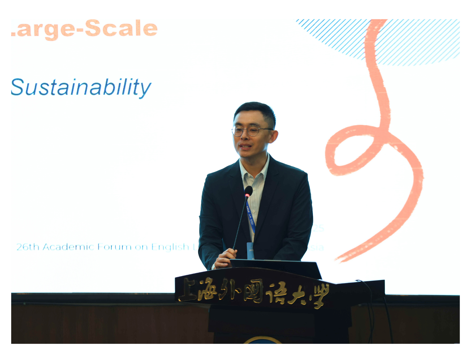 A person stands at a podium with a presentation screen displaying the word "Sustainability" in the background.