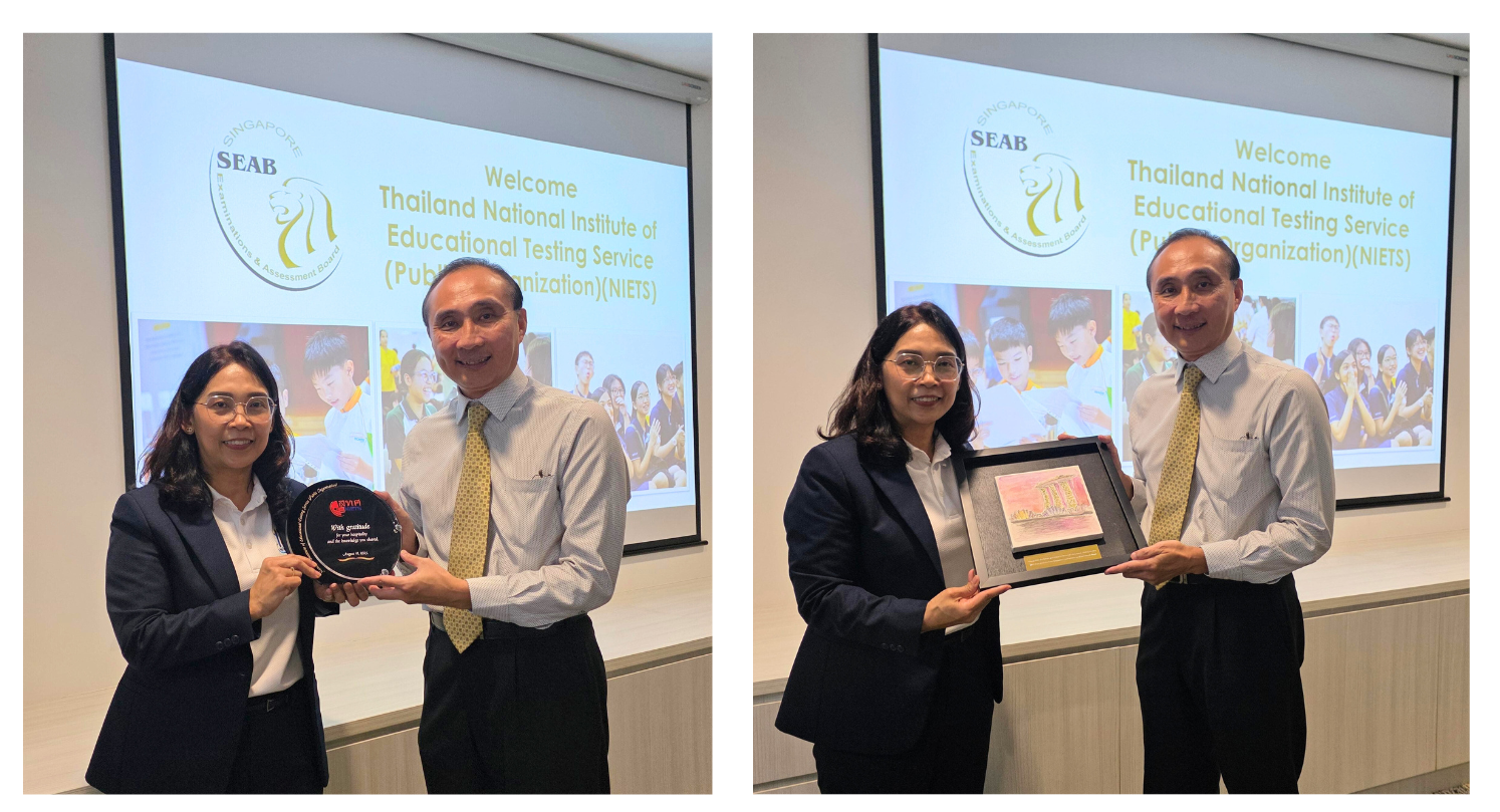 Two individuals stand in front of a presentation screen holding awards from Singapore's SEAB and Thailand's NIETS.