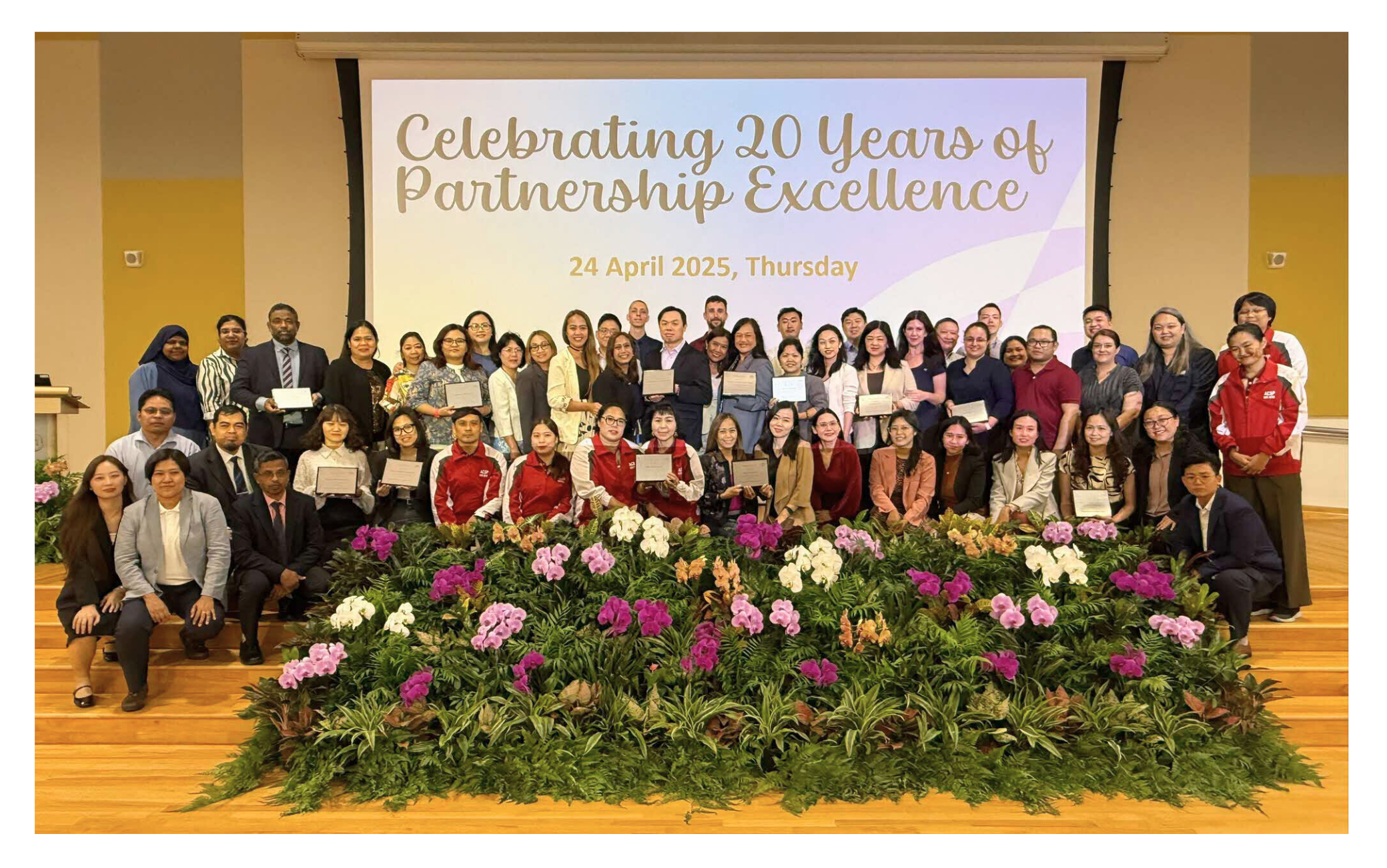 Large group of people holding certificates, standing on stage with "Celebrating 20 Years of Partnership Excellence" written behind.