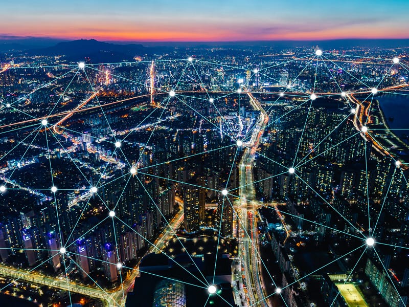 Aerial night view of a lit city with glowing network connection nodes and lines overlaid across it.