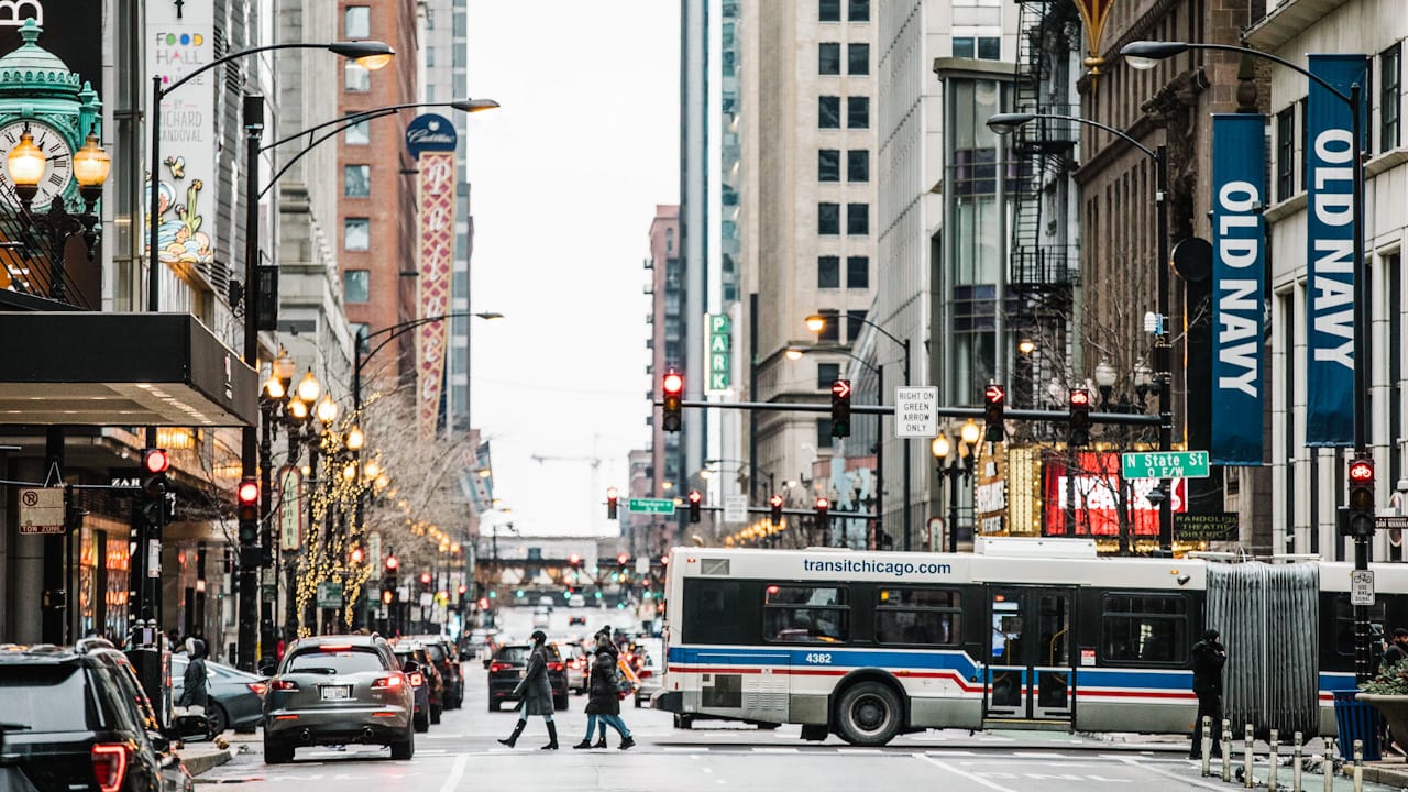 Busy Chicago downtown street with a transit bus, pedestrians crossing, tall buildings, and an Old Navy banner.