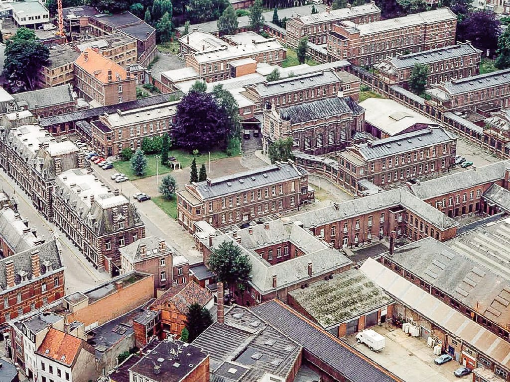 Aerial view of a dense European city block with red brick buildings, courtyards, trees, and roads.