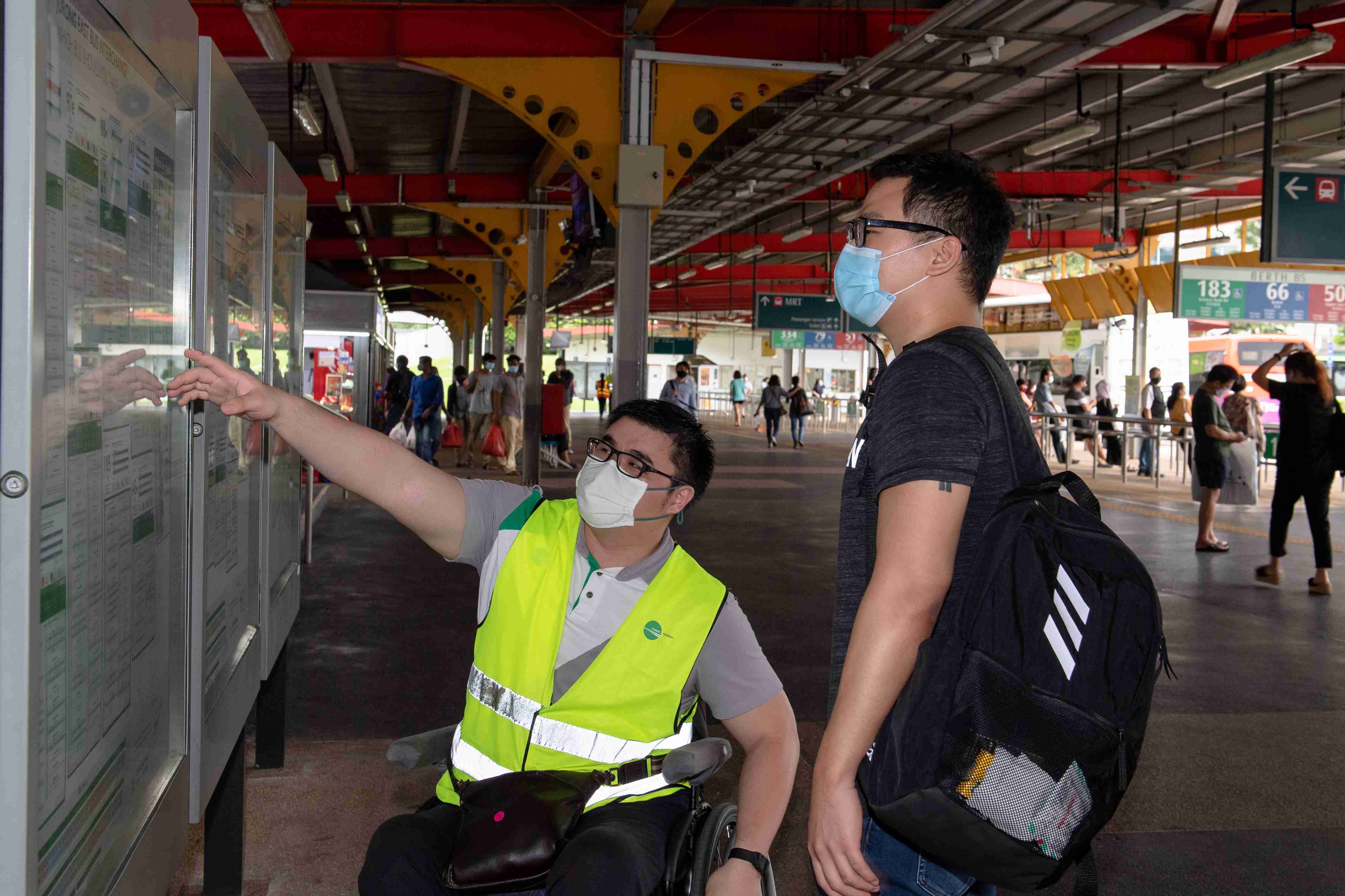 Kishon sitting in a wheelchair assisting a commuter with wayfinding