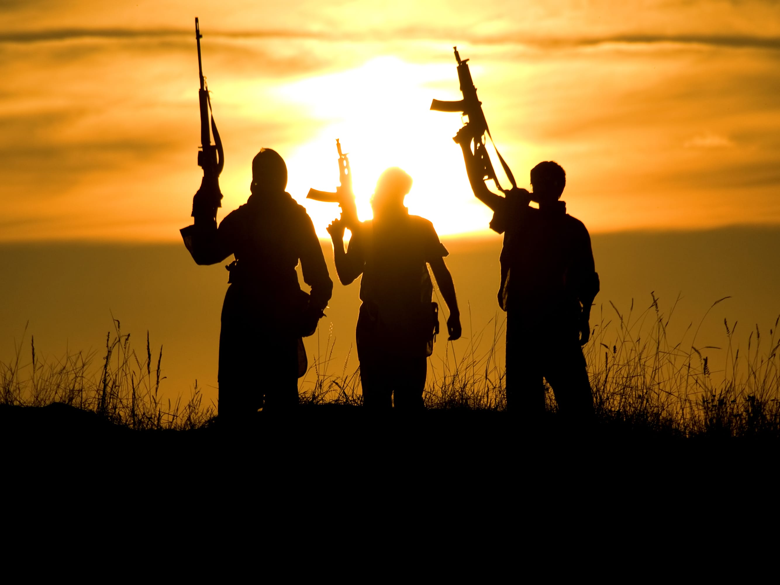 People with guns, silhouetted by the sun