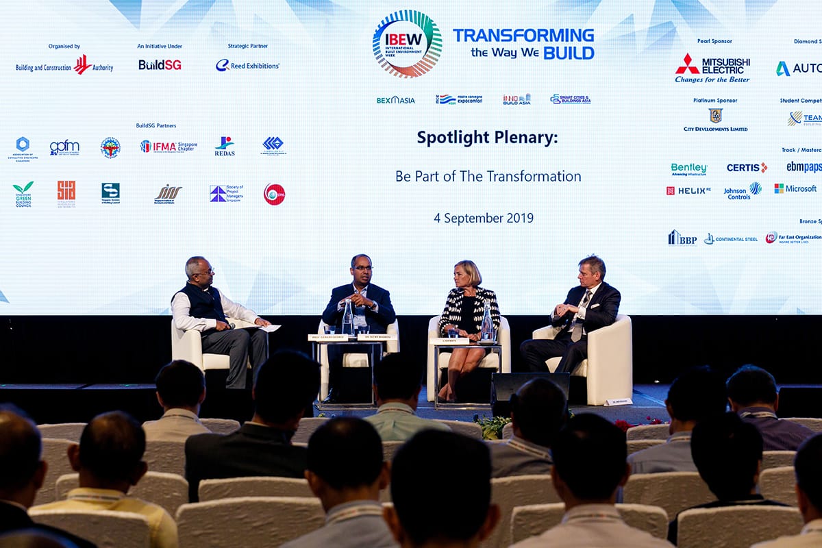 Four speakers on stage at "Transforming the Way We Build" conference in front of audience. Logos above.