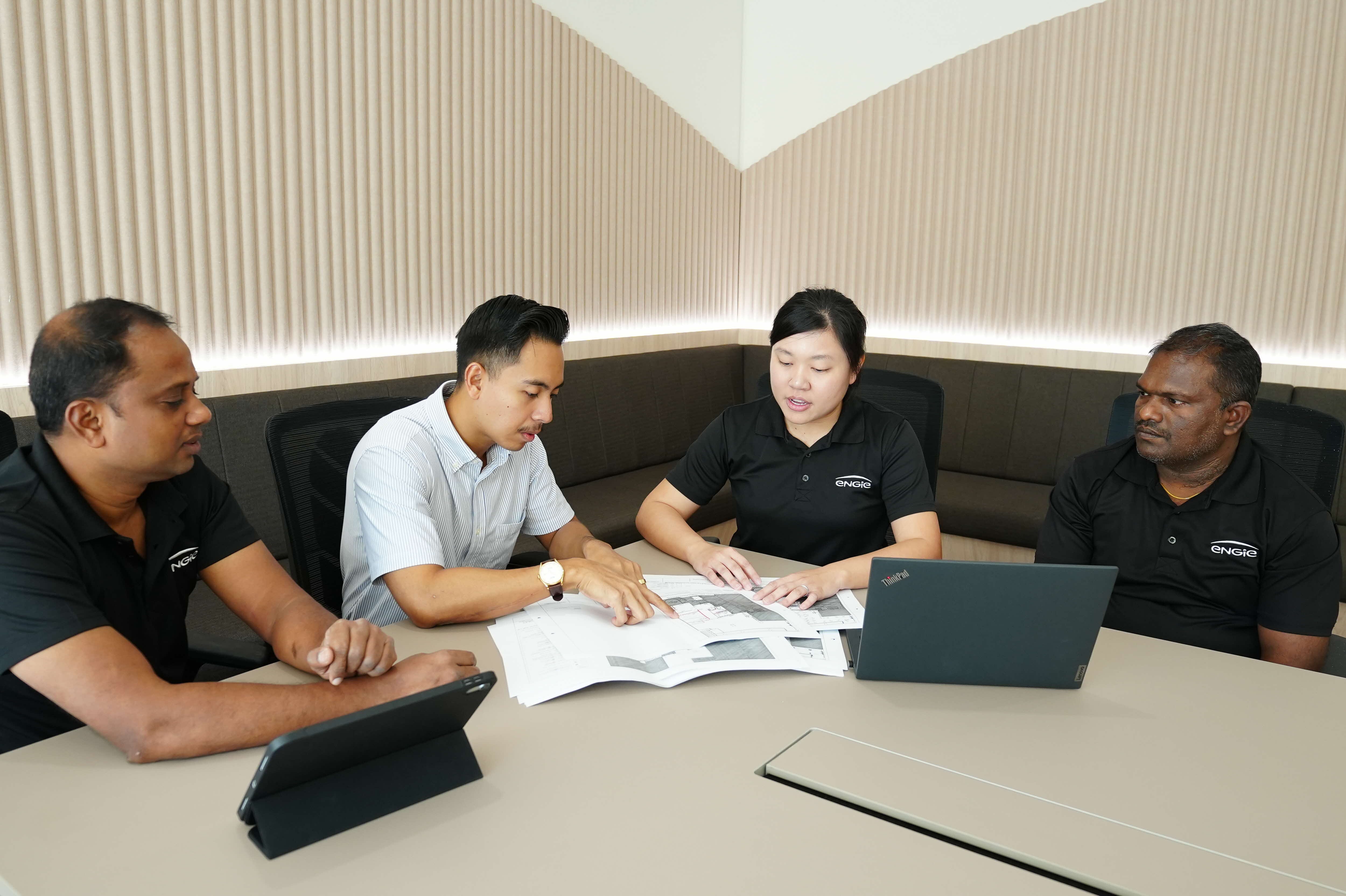 Four ENGIE employees review plans on a table with a ThinkPad laptop and a tablet.