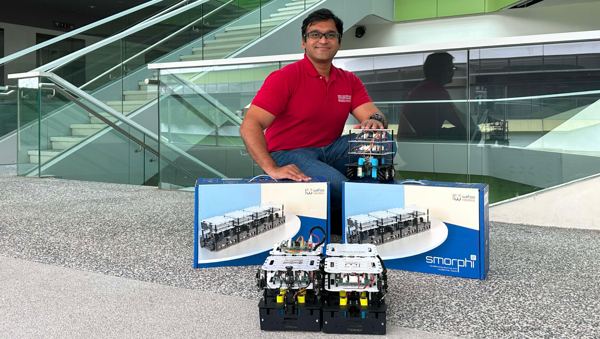 Man with Weefaa Robotics smorph2 sets and robots near modern glass stairs.