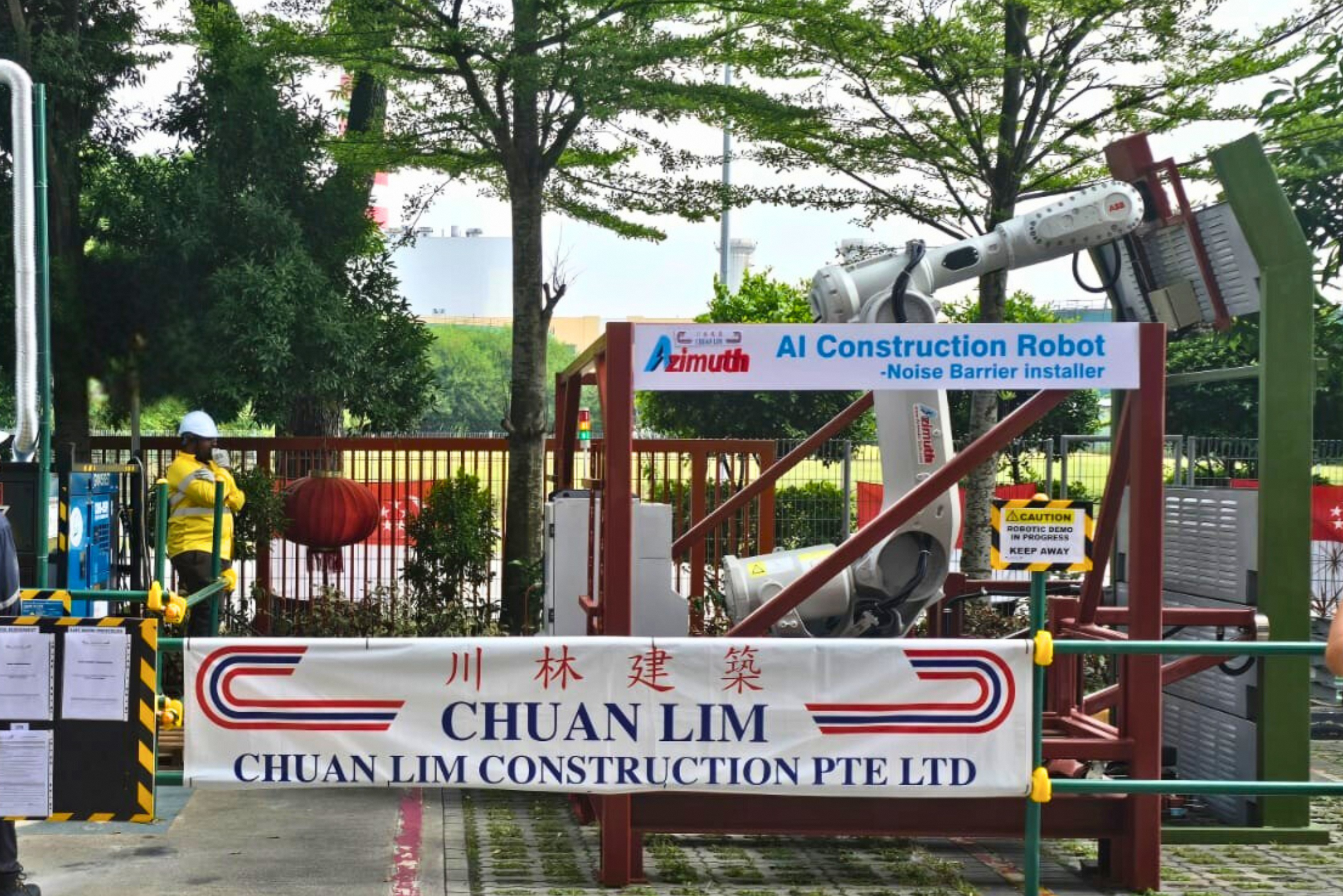 ABB robot arm with Azimuth sign, and banner for Chuan Lim Construction, surrounded by safety barriers.