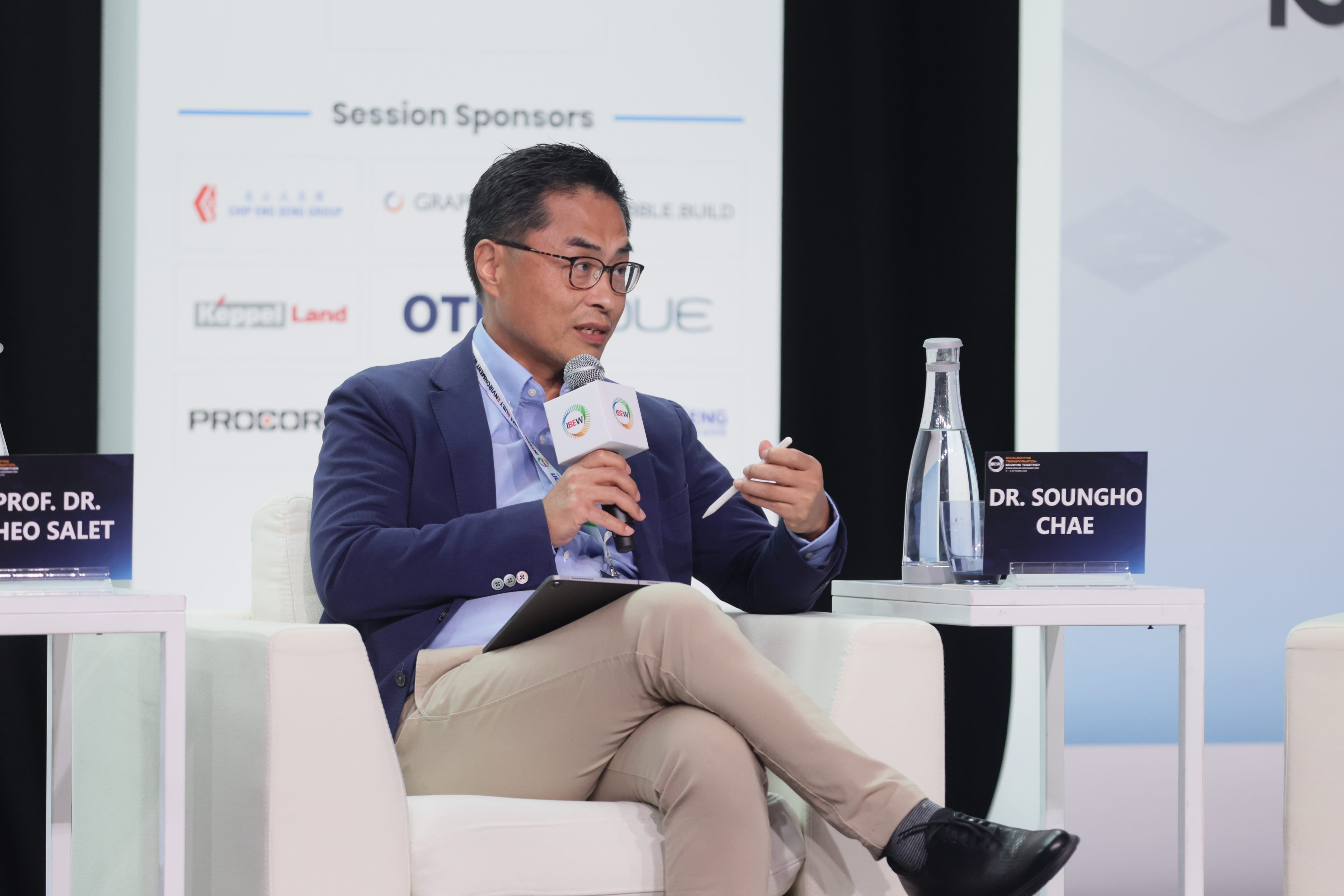 Dr. Soungho Chae sits on stage speaking into a microphone, holding a tablet and pen.