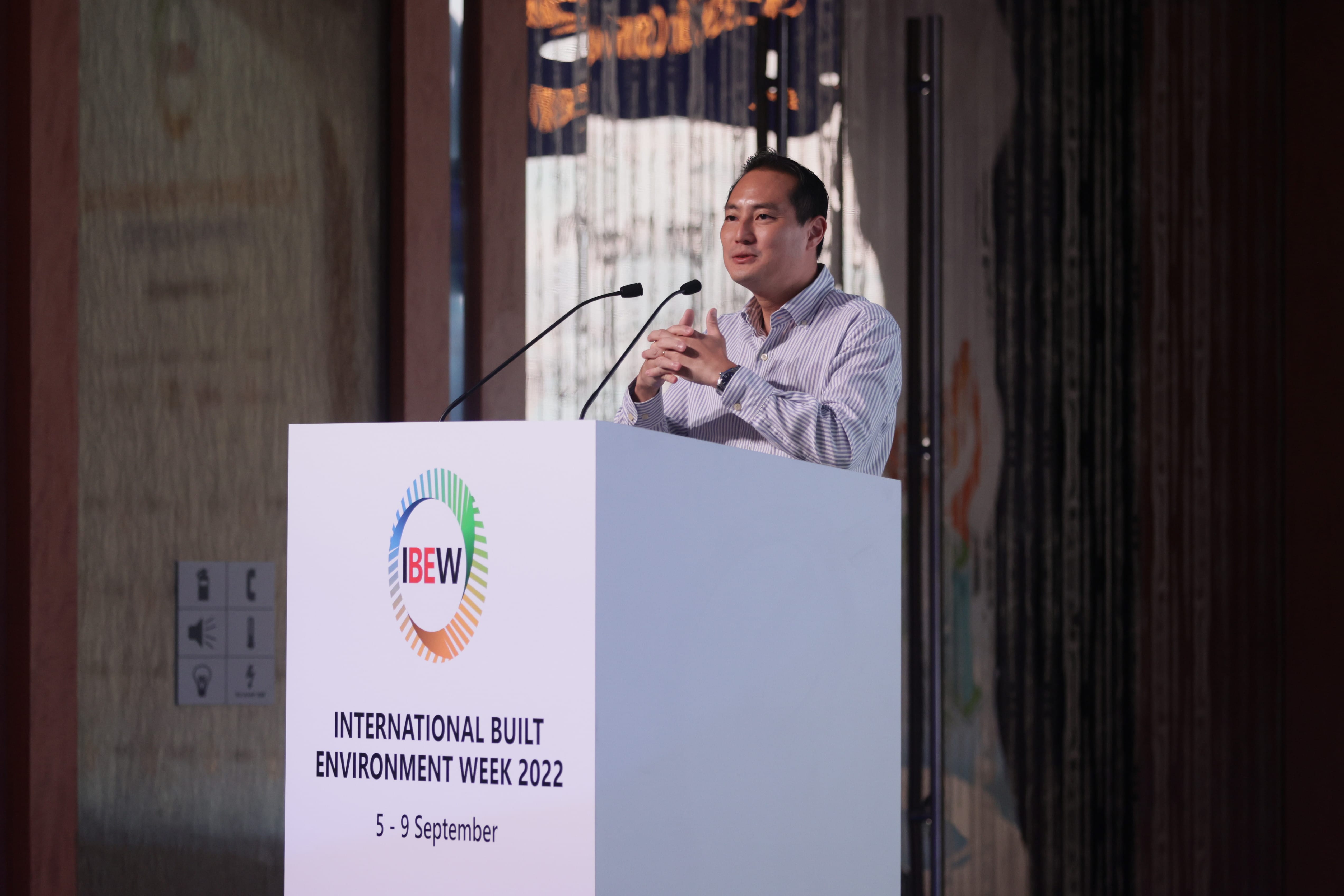 Man at podium for "International Built Environment Week 2022" with IBEW logo. Microphones present.