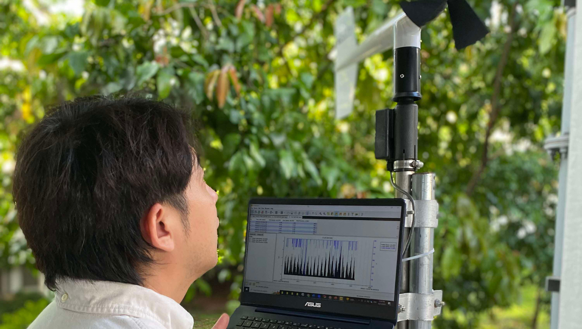 Person views Asus laptop showing data charts, next to a weather vane mounted on a pole.