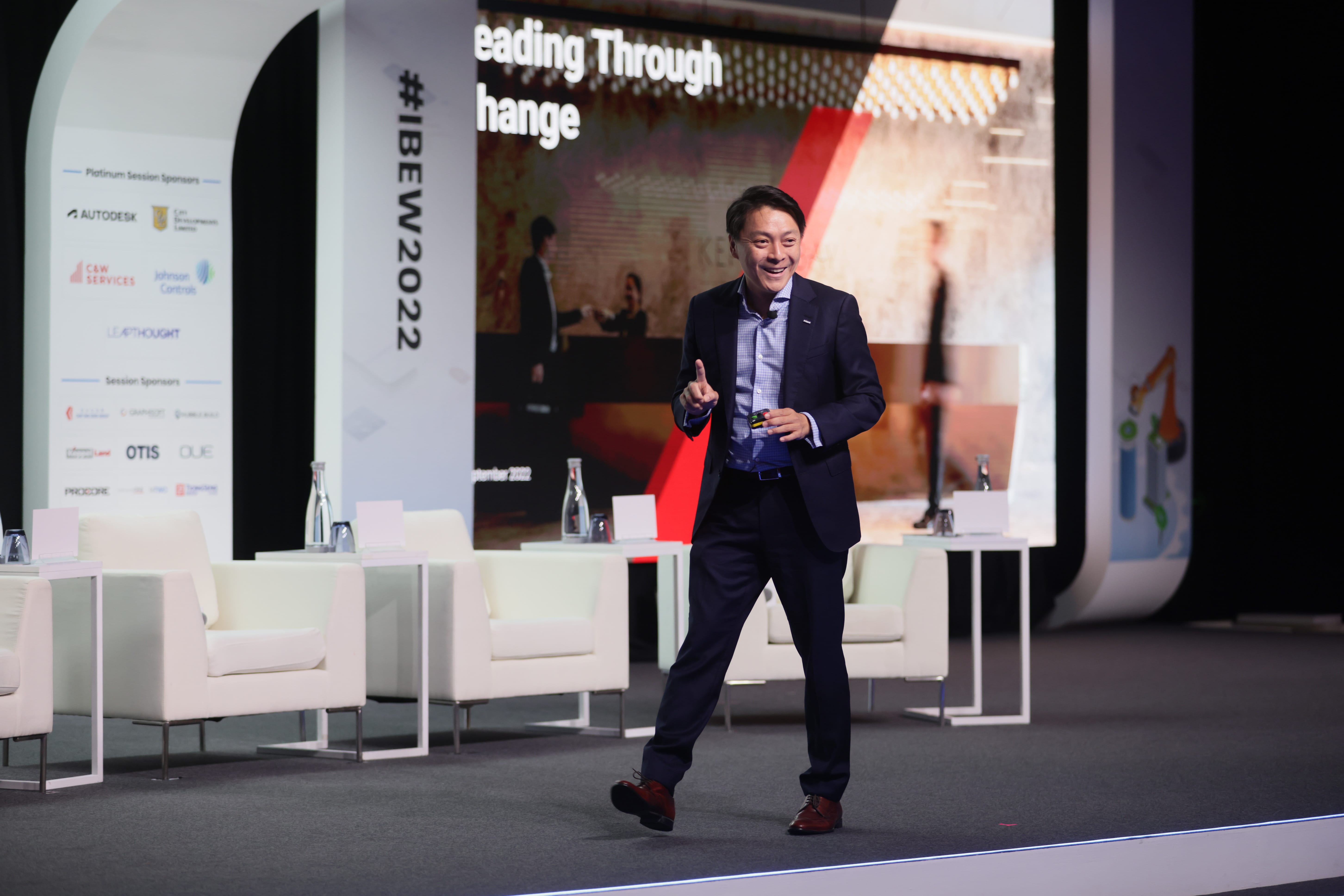 Asian man in a suit presents on stage at #IBEW2022, with sponsor logos like Autodesk visible.