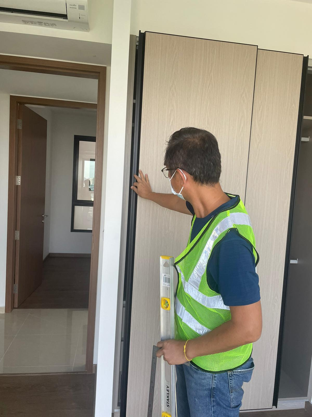 Worker with Stanley level installing wood paneled sliding doors, wearing safety vest.