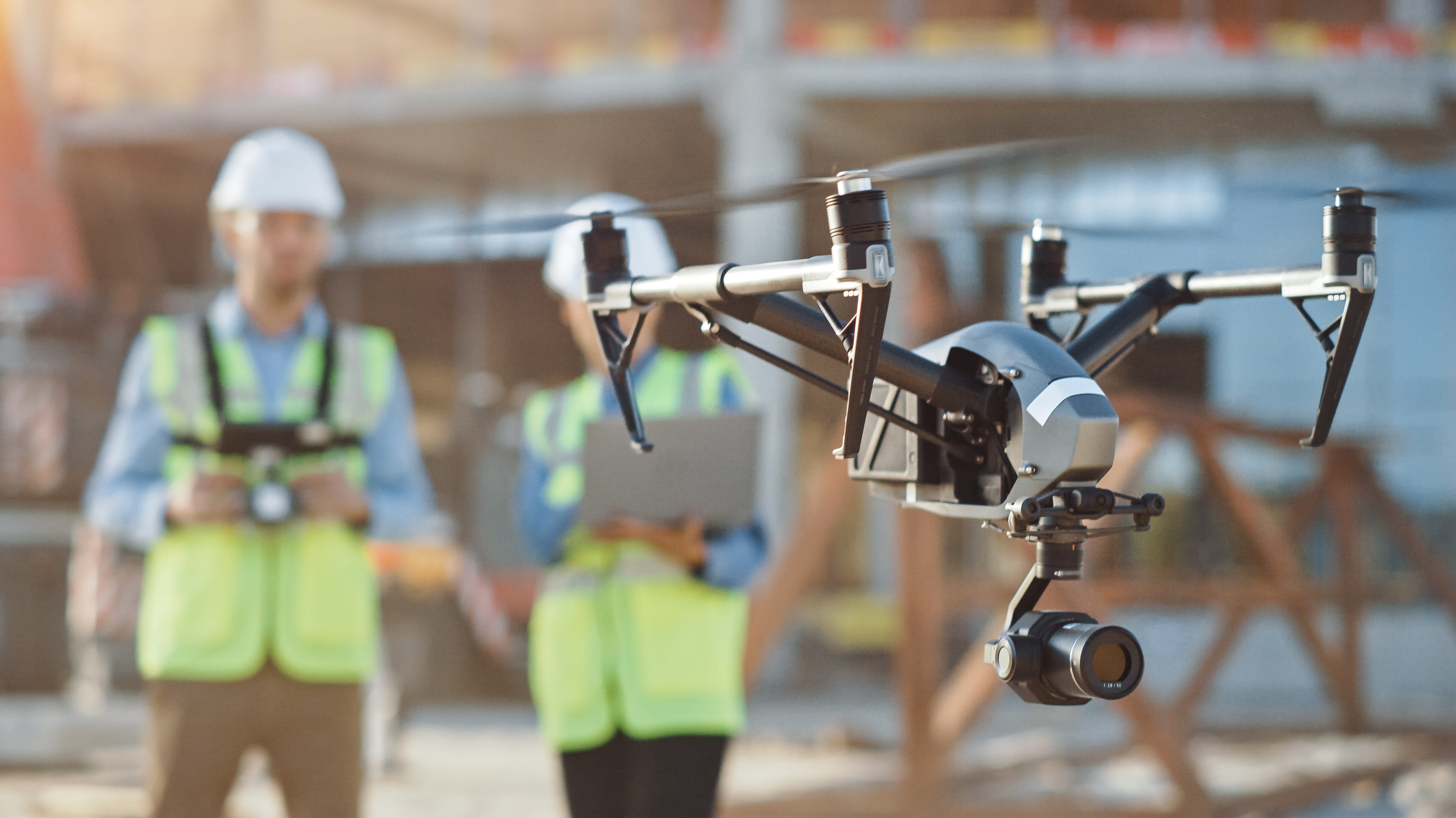 DJI Inspire drone hovers at a construction site; workers in hard hats and vests visible.