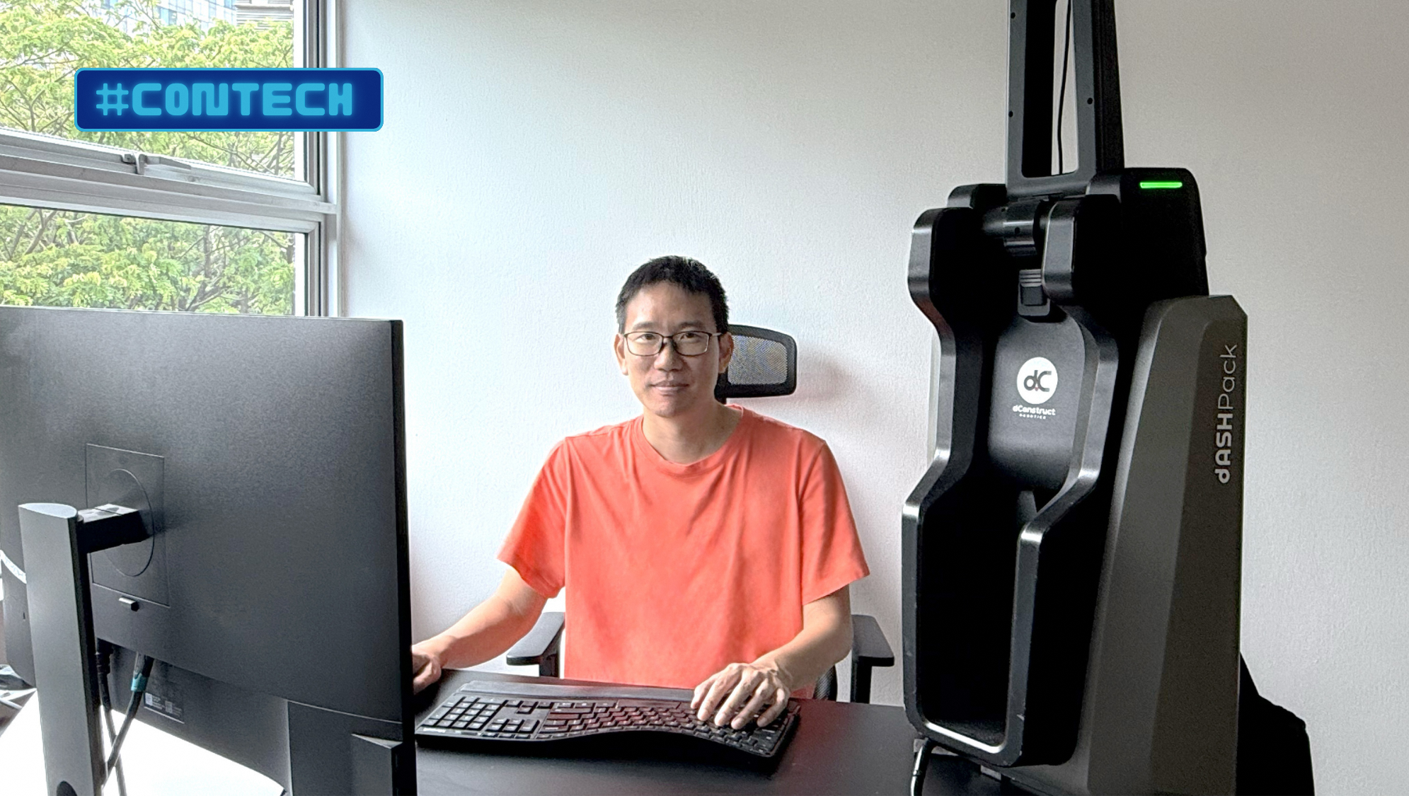 Person at desk with #ConTech label, monitor, keyboard, and dConstruct DASHPack device.