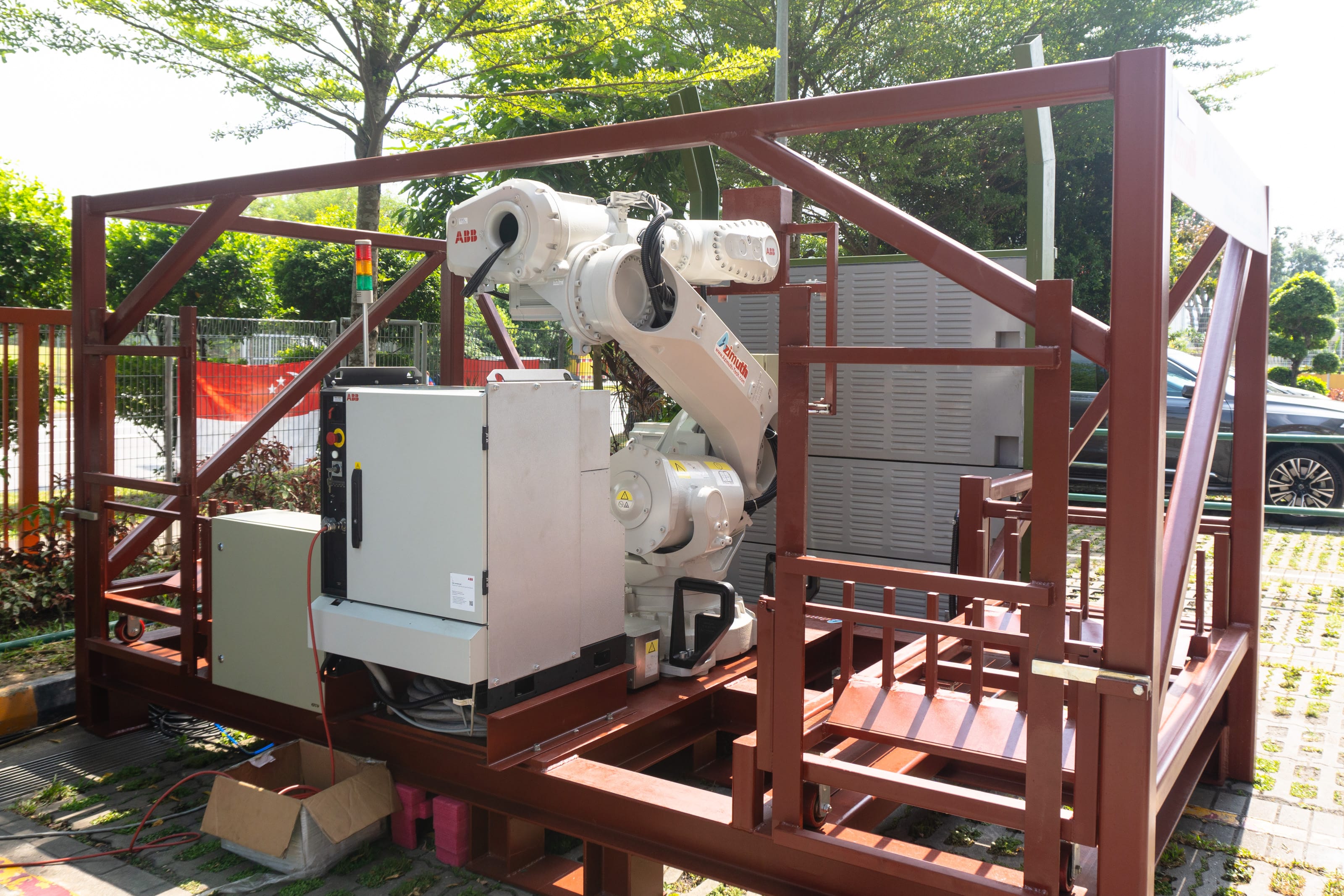 ABB industrial robot arm and control box mounted on a brown steel frame outdoors.