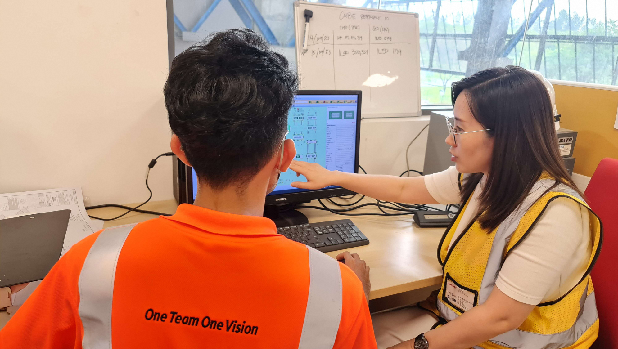 Two people in safety vests look at a Philips monitor displaying a schematic diagram.