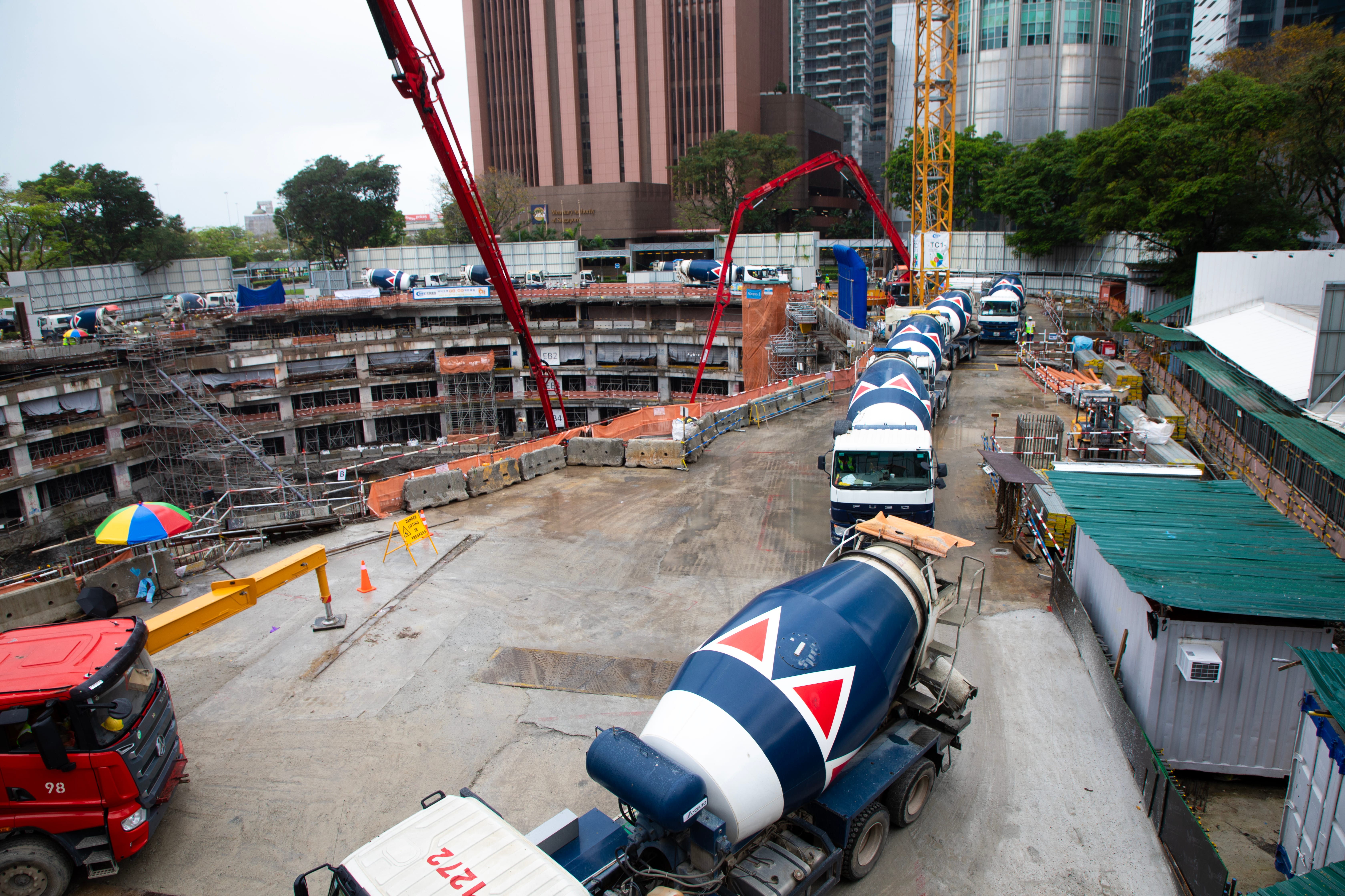 Construction site with concrete foundation, mixer trucks, and cranes against a city skyline.