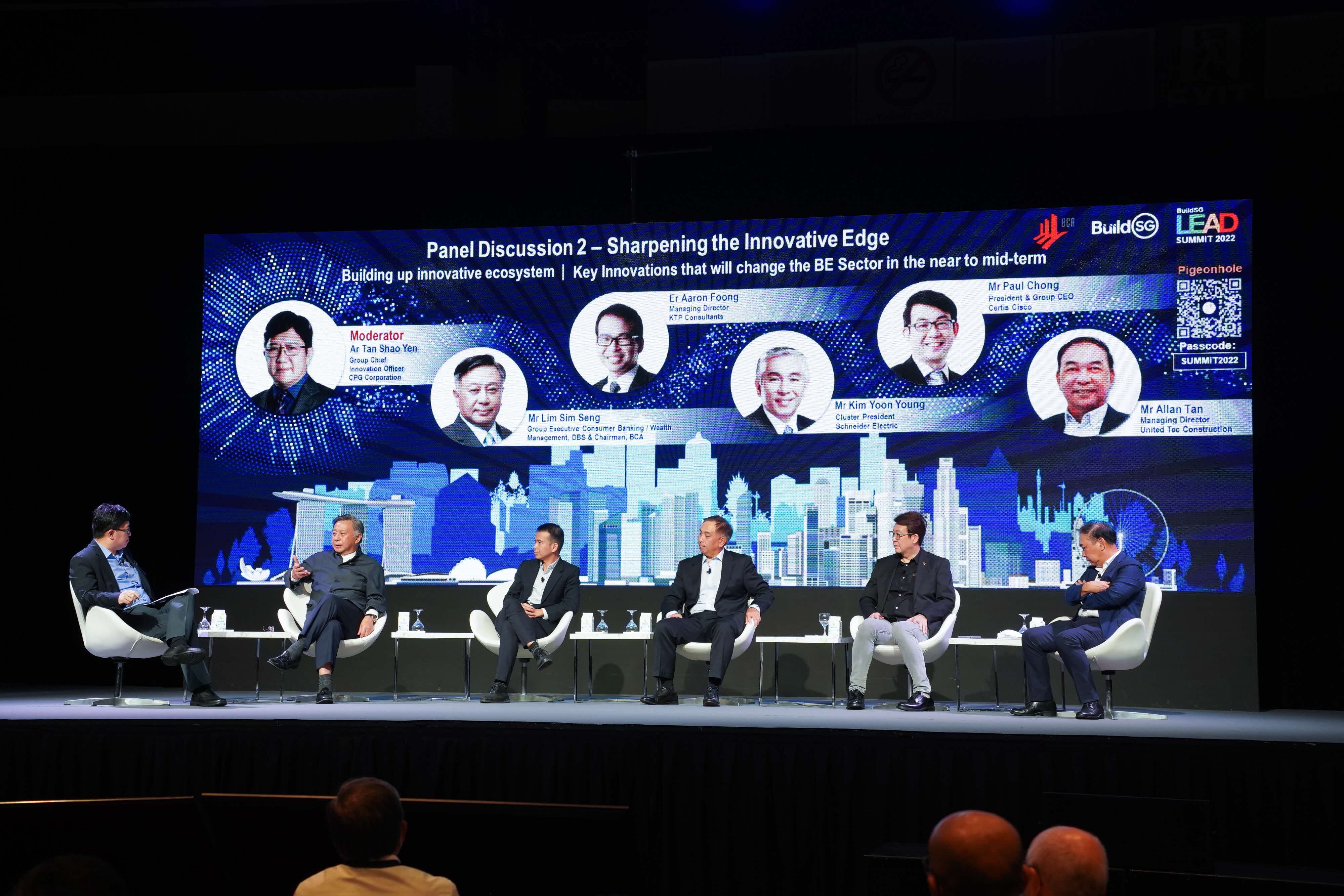 Panel discussion onstage with seven seated panelists and a presentation screen backdrop.