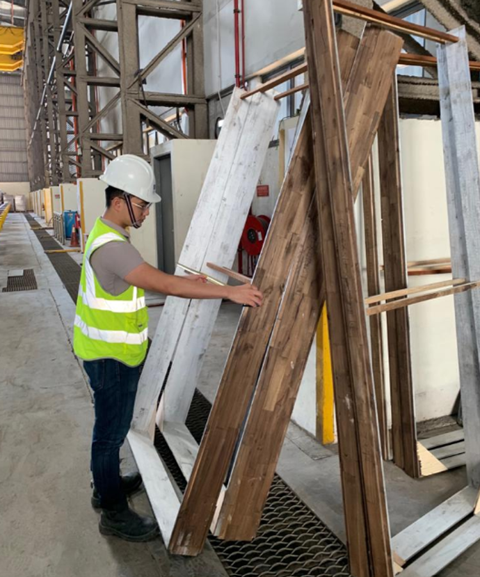 Worker in hard hat and safety vest measuring wood frames in an industrial setting.