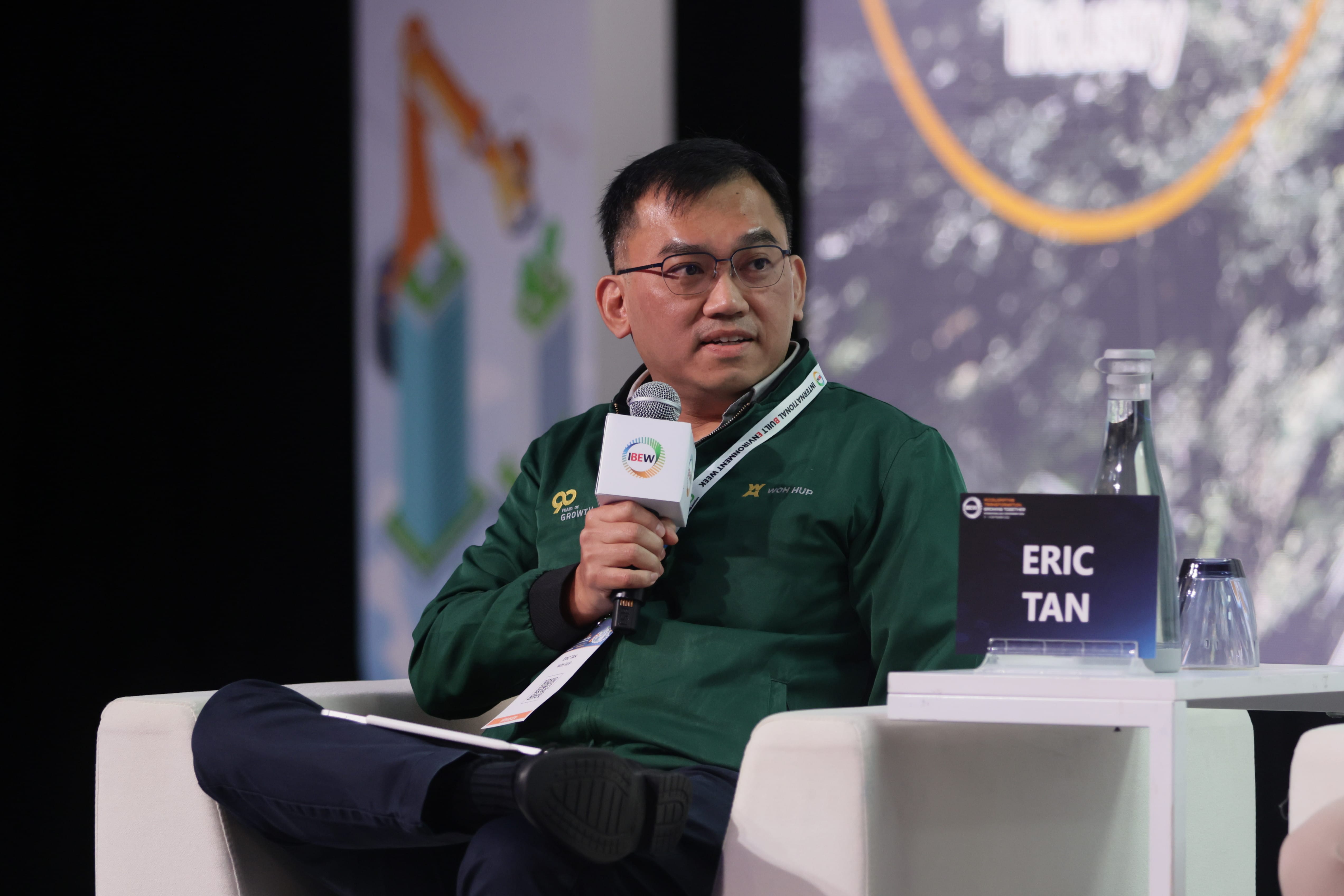 Eric Tan in green jacket with IBEW mic sits in white chair at event with "Eric Tan" nameplate.