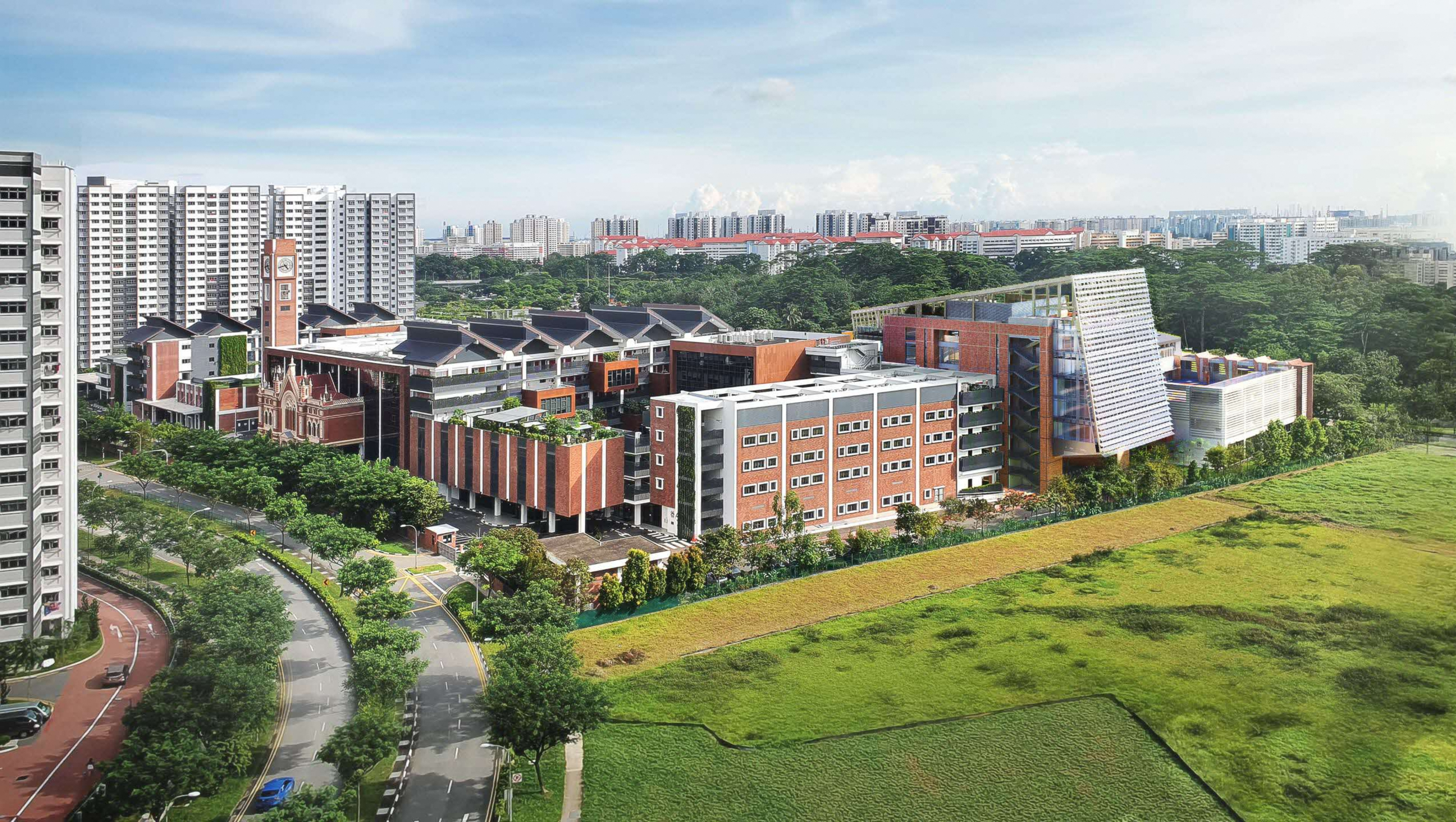 Cityscape with modern brick buildings, clock tower, and green field in the foreground.