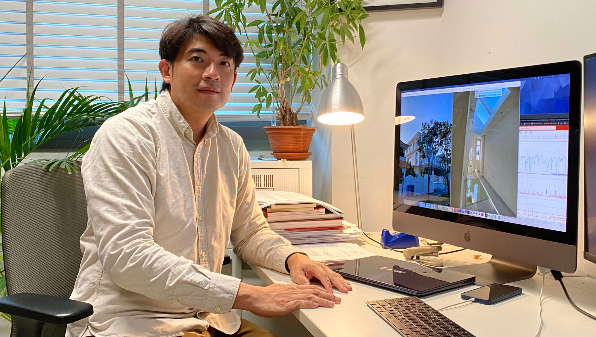 Person sits at desk with Apple computer showing building design and charts.