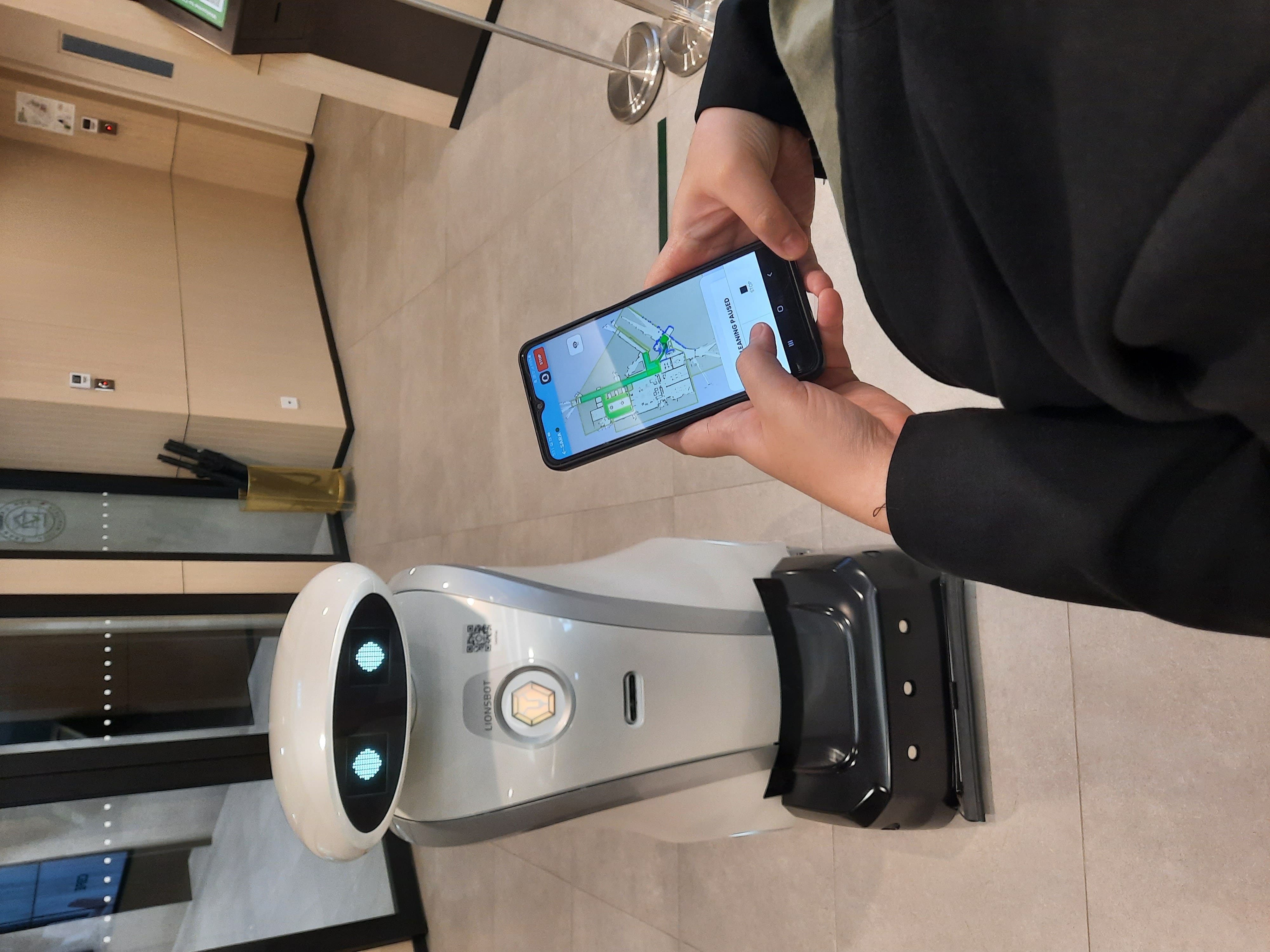 Person holding phone with map app near Lionsbot robot.