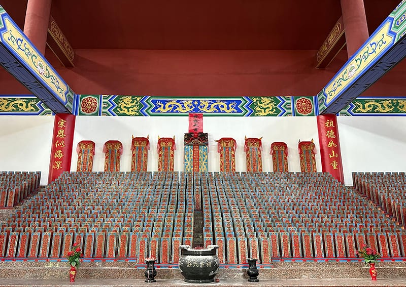 An ornate Chinese temple interior with rows of red placards, decorative pillars, and a central altar with incense burners.