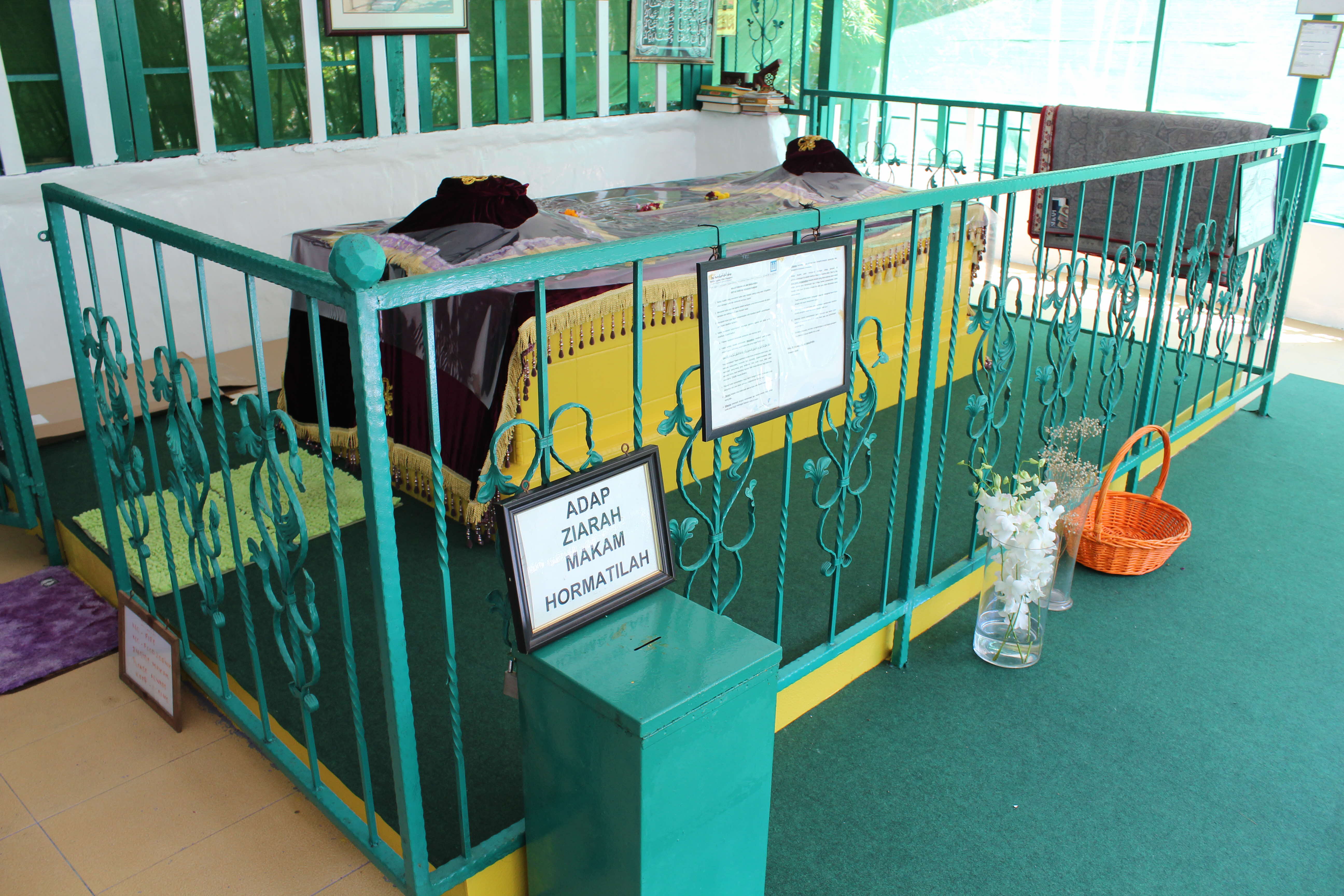 A well-maintained grave surrounded by a teal metal railing, covered with cloths and adorned with flowers and books.