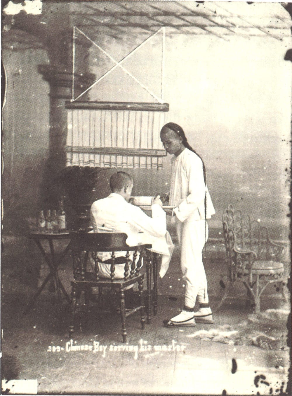 A Chinese houseboy serves his European master who is sitting under a punkah (a large screenlike fan hung from the ceiling and operated by a servant or by machinery). Photo by G. R. Lambert & Co., 1890. Courtesy of the National Museum of Singapore, National Heritage Board.