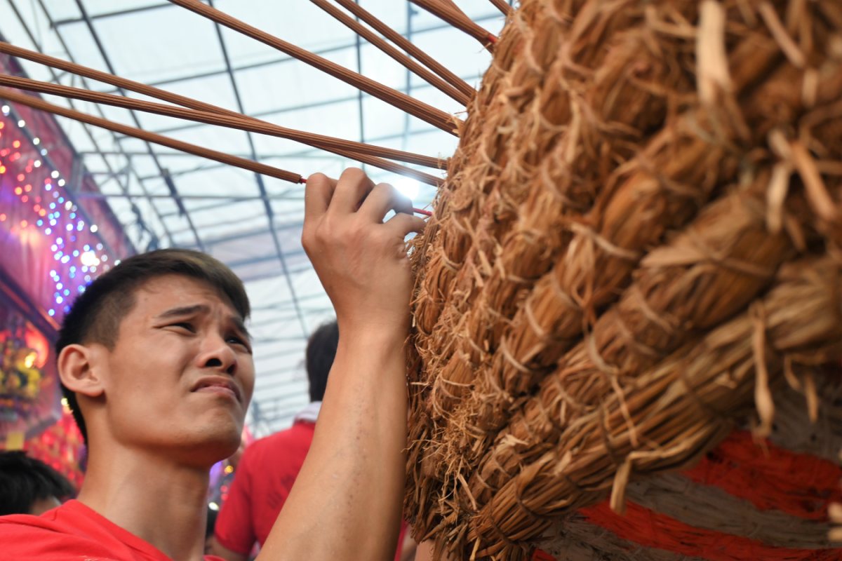 A devotee carefully inserting a lit joss stick into the dragon, 2023. Courtesy of Yeo GT.