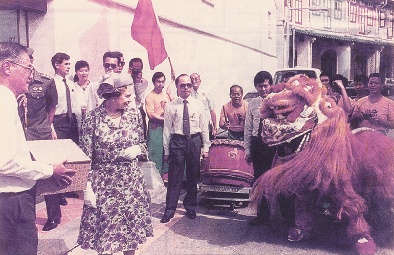 Queen Elizabeth II being greeted by a Golden Lion Dance performance by the Chin Woo lion dance troupe during her visit to Tanjong Pagar Conservation Area, 1989. Donated by Singapore Chin Woo (Athletic) Association. Collection of the National Library, Singapore.