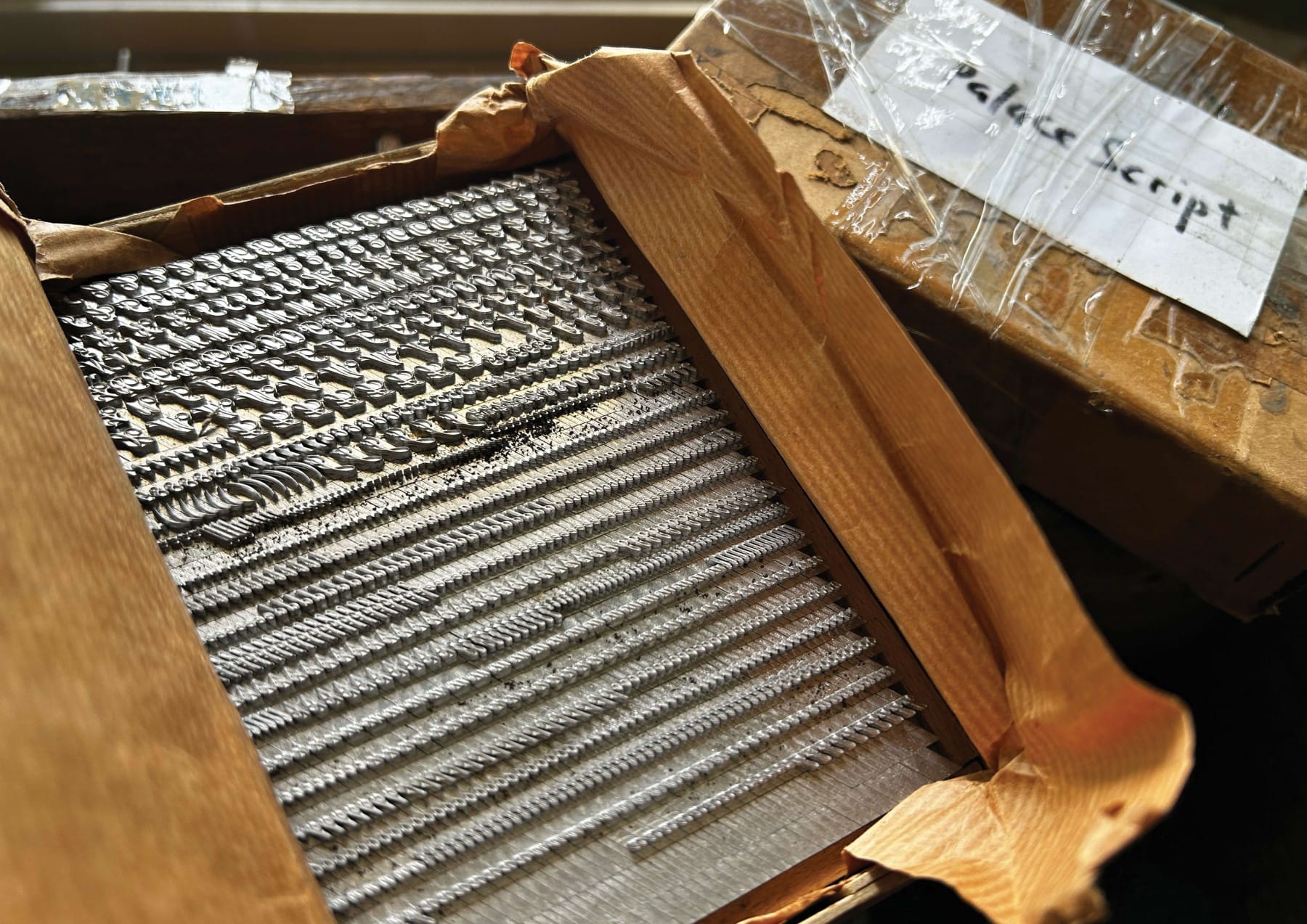 Box containing metal types for printing covered in packing paper with a label saying "Palace Script".