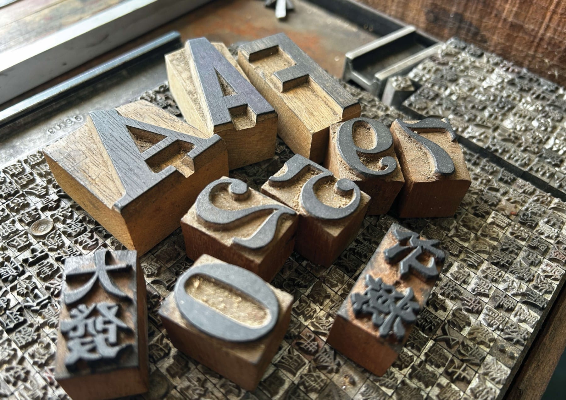 A collection of wooden printing blocks with various letters and Chinese characters arranged on a metal surface.