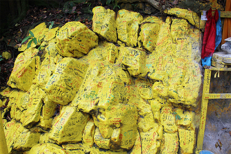 Lottery numbers are scrawled over the painted rocks at the entrance to the keramat at the top of the stairs, 2022. Courtesy of William L. Gibson.