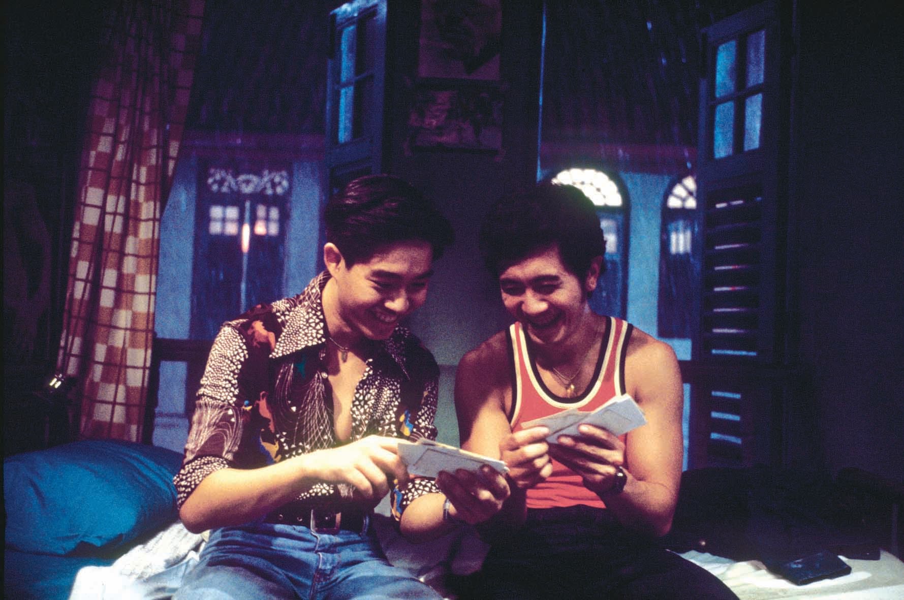 Two people sit close together in a dimly lit room holding multiple pieces of white paper.