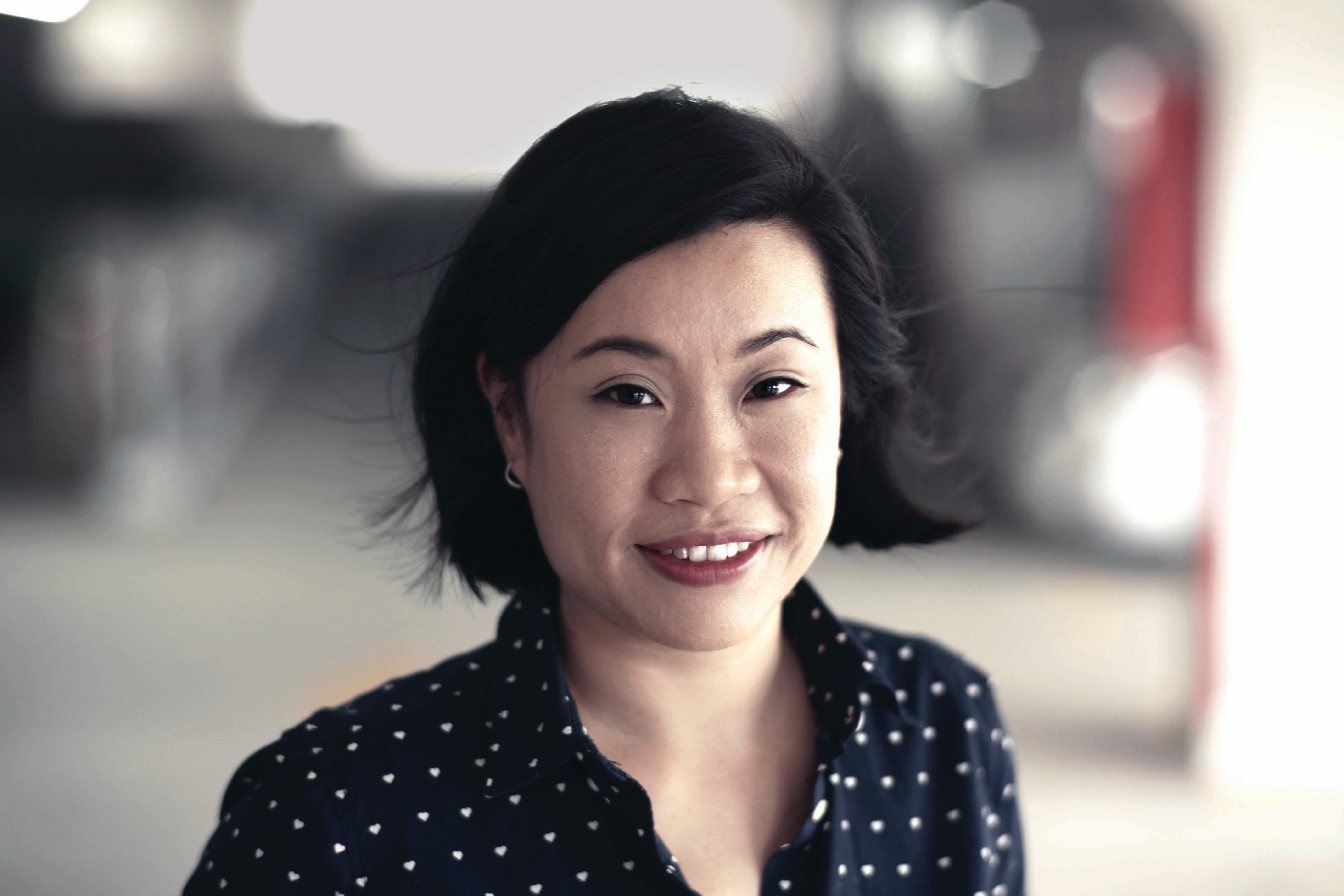 A person with short black hair wears small hoop earrings and a black shirt with white heart patterns.