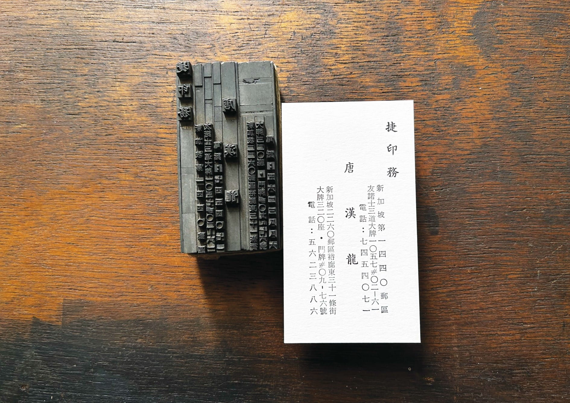 A block of traditional Chinese movable type printing alongside a printed card on a wooden surface.
