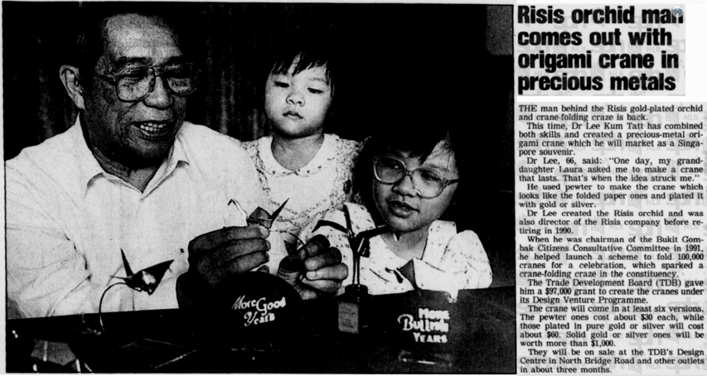 Three people sit at a table holding metallic origami cranes with text detailing a new product launch beside them.