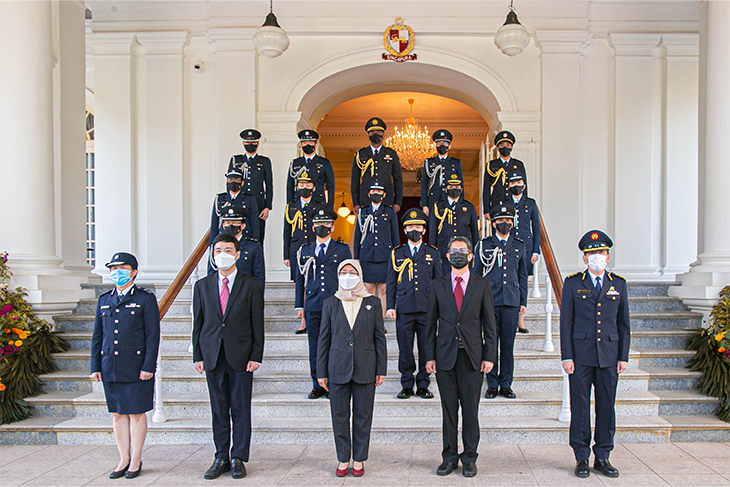 Group of people on steps in front of white building, some in suits, others in police uniforms.