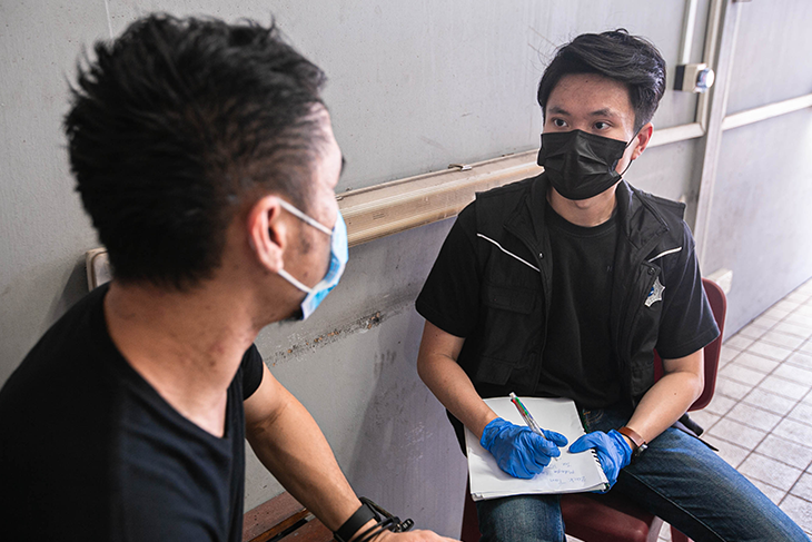 Two masked men: one wearing blue gloves and taking notes from the other.