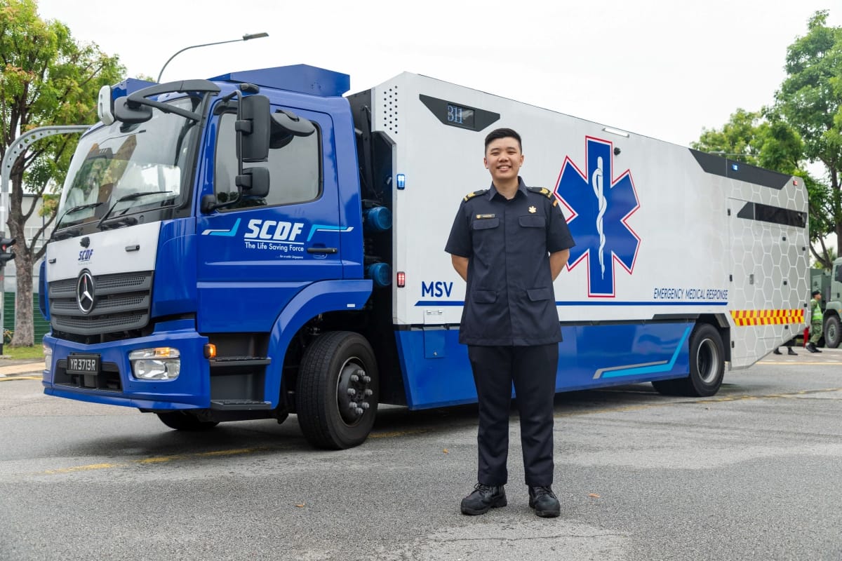 SCDF officer stands before a blue and white Emergency Medical Response vehicle.